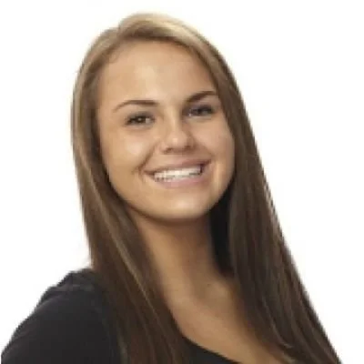 A smiling young woman with long brown hair wearing a black top against a white background.