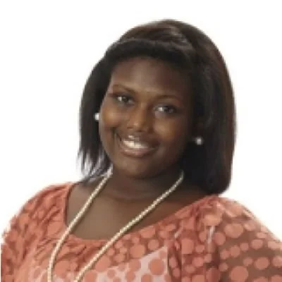 A woman with dark hair and earrings, smiling, wearing a pink patterned dress and a pearl necklace against a white background.