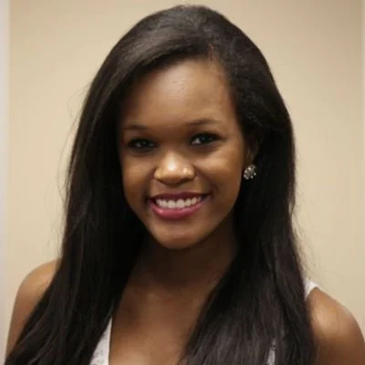 Portrait of a young woman with long black hair, wearing earrings, smiling, and dressed in a white top.