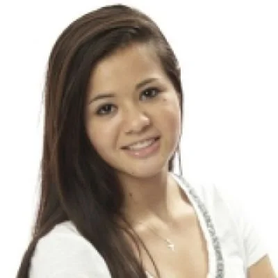 A young woman with long dark hair smiling at the camera, wearing a white top with a necklace.