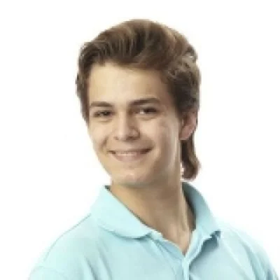 Young man with brown hair smiling, wearing a light blue polo shirt, against a plain white background.