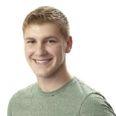 A smiling young man with short blonde hair wearing a light green t-shirt against a white background.