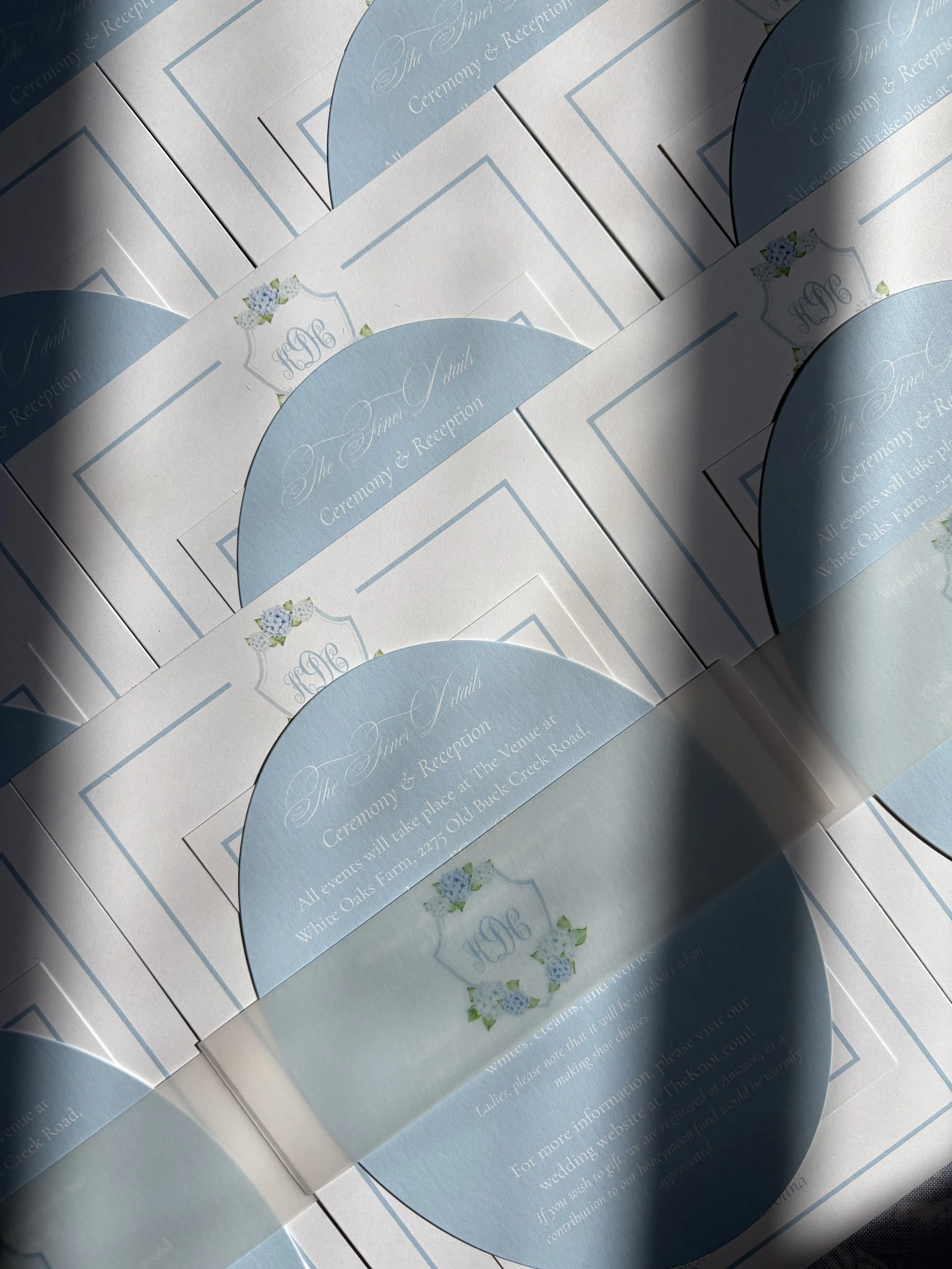 Multiple wedding invitations with a light blue and white color scheme, decorated with small floral illustrations, arranged overlapping each other on a flat surface.