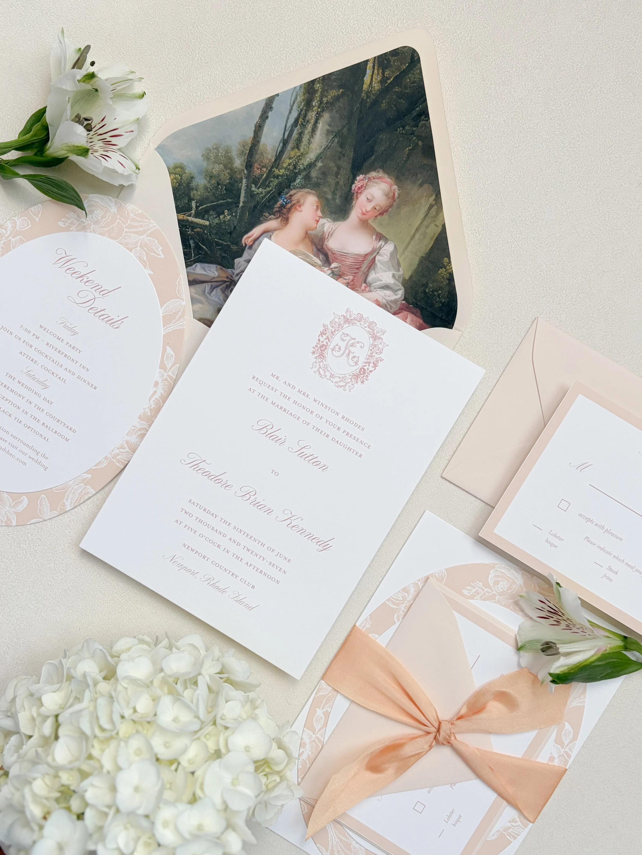 Wedding invitations and floral arrangements on a white surface, featuring a romantic painting of two women, white hydrangeas, and a peach-colored gift box with a ribbon.