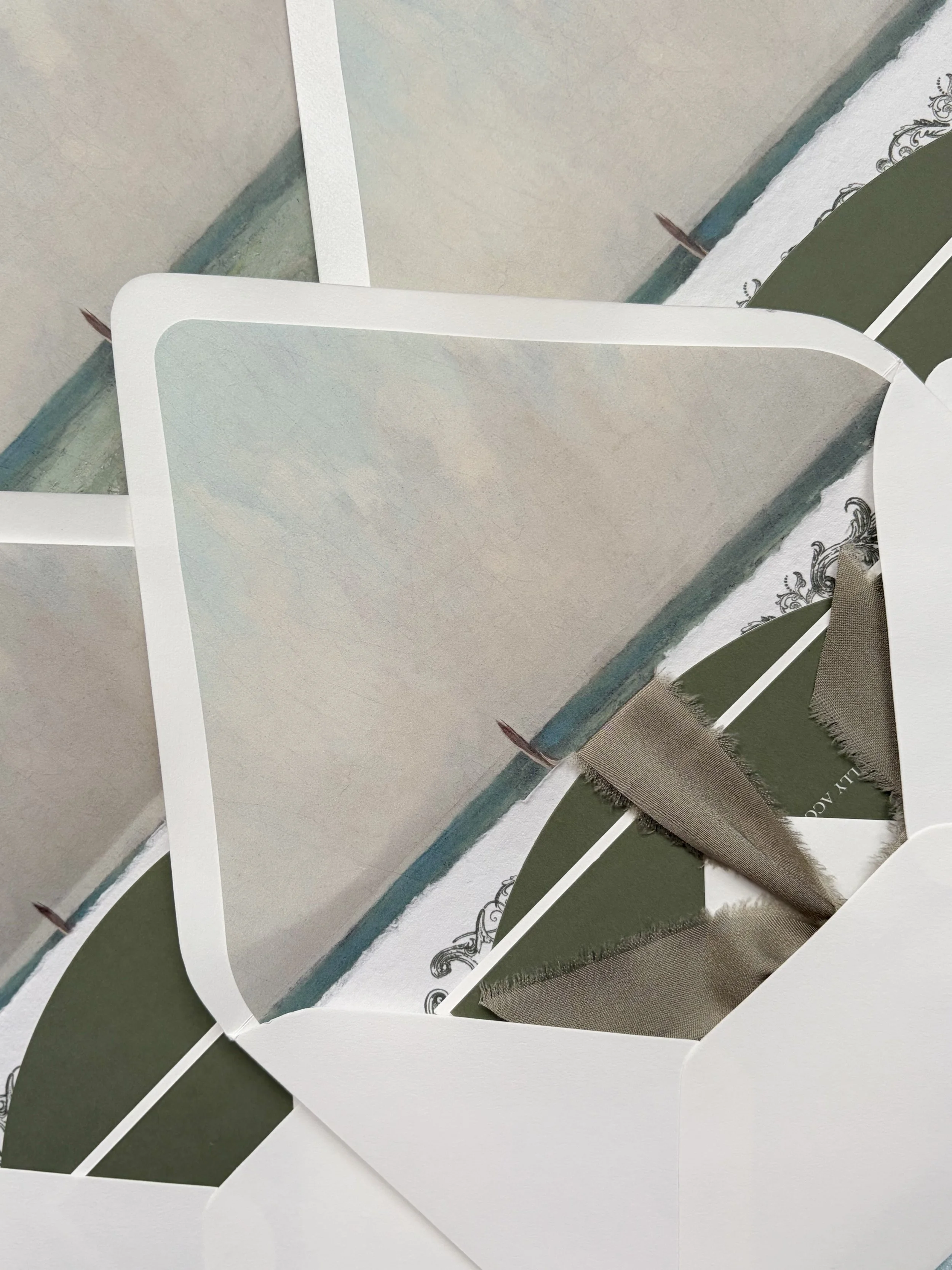 Close-up photo of fabric samples and paper sheets with color and texture variations, some with decorative borders and embroidery, on a flat surface.