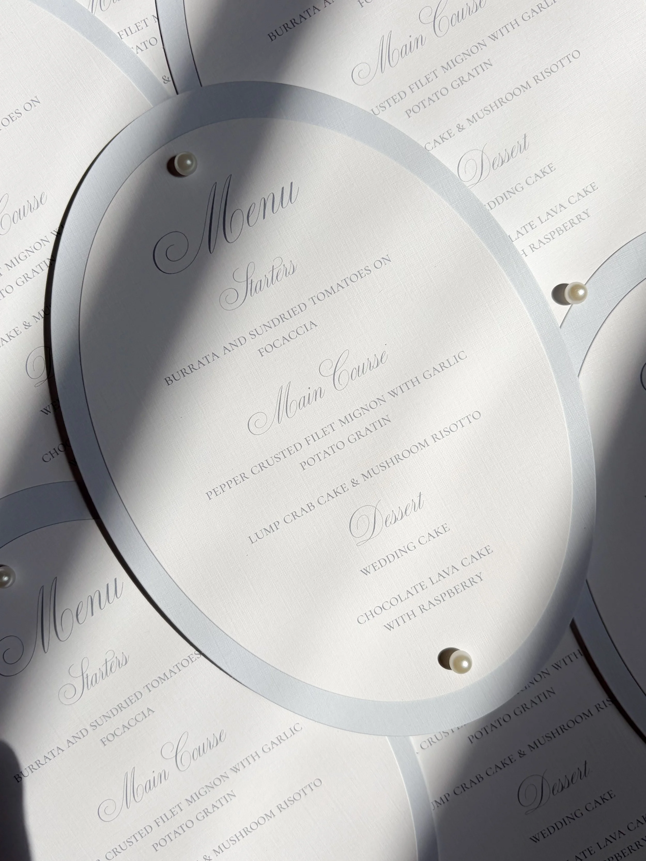 Close-up of a wedding menu with elegant cursive and serif fonts, pinned with pearl-headed decorative pins.