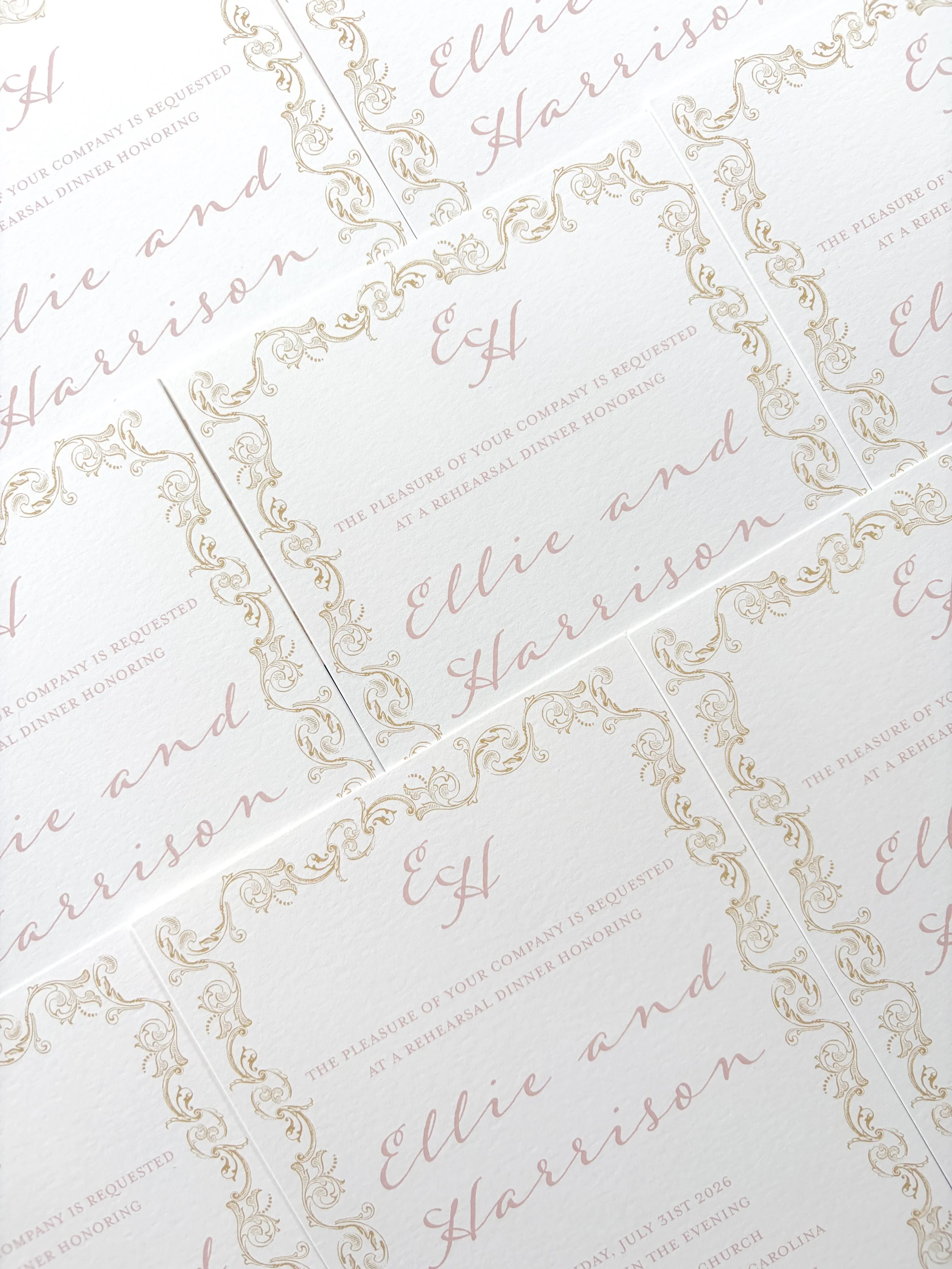Multiple elegant, white and gold wedding invitations with ornate decorative borders and pink cursive text that says 'Elijah and Harrison'. The invitations contain details about a wedding rehearsal dinner on July 31st, 2026, at 6:00 pm at a church in North Carolina.