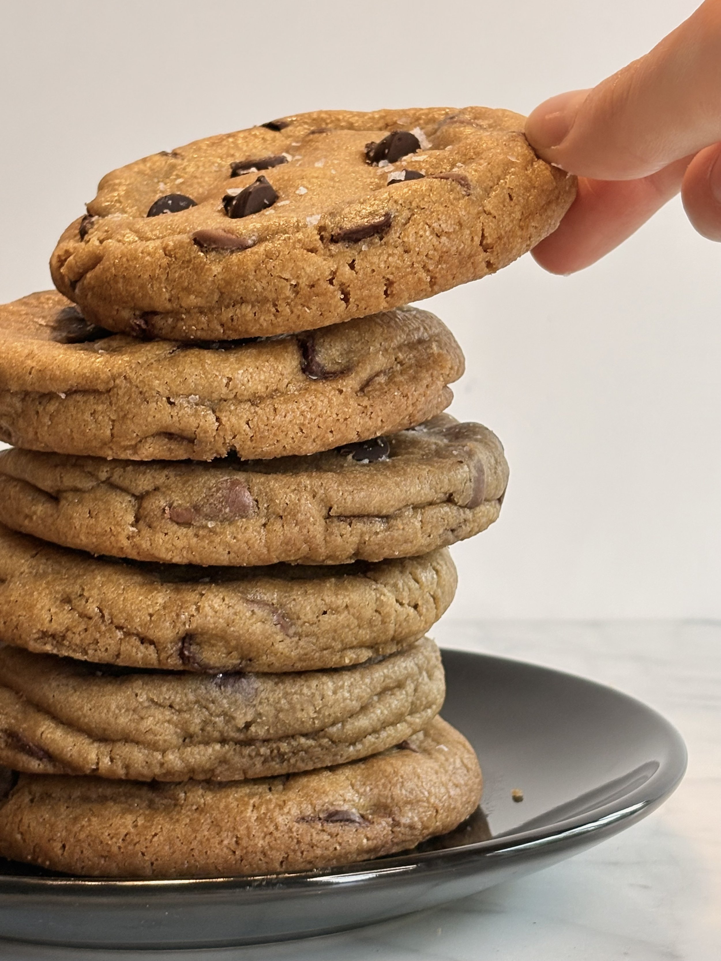 A stack of chocolate chip cookies on a black plate with a plain white background