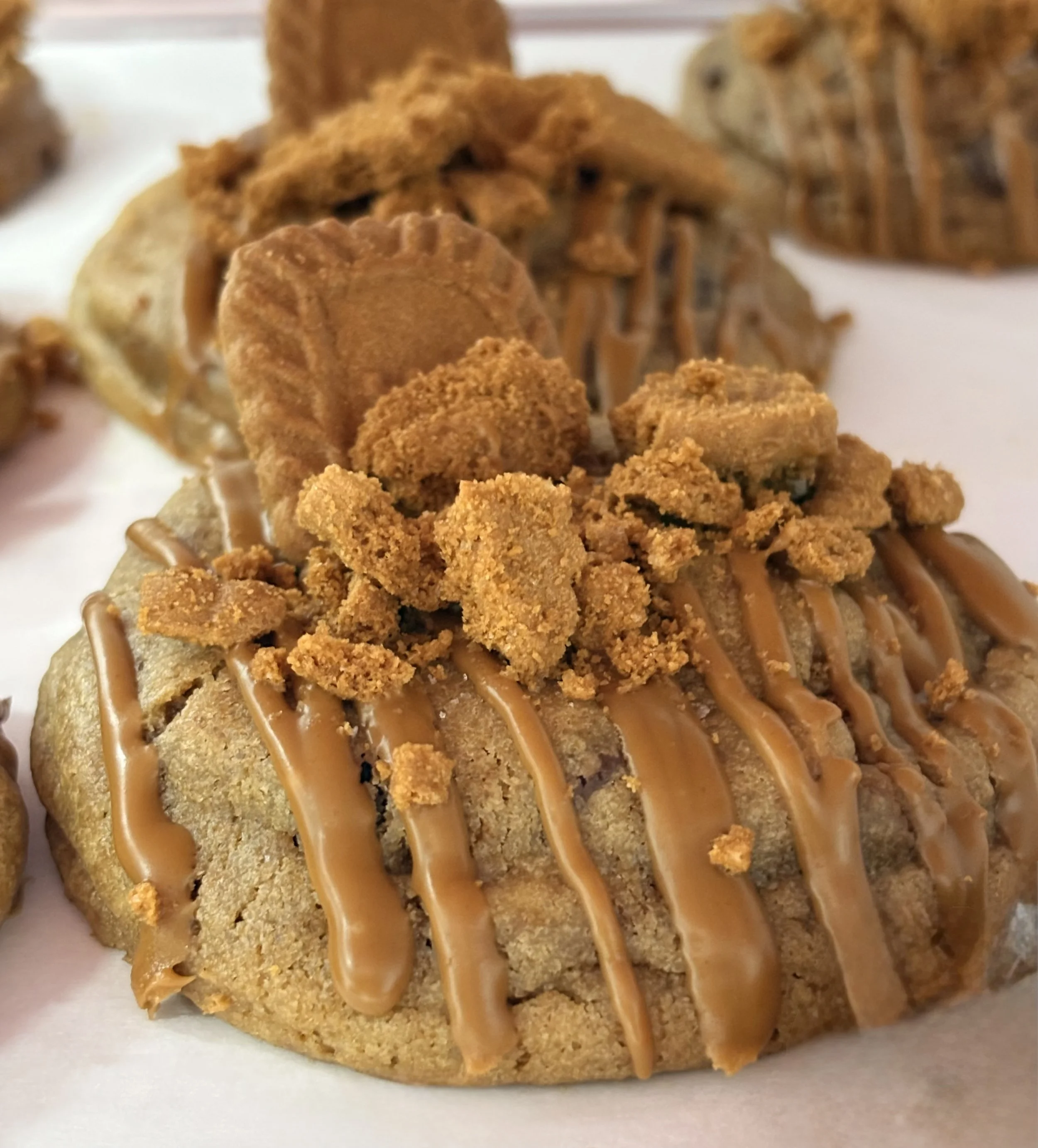 Close-up of a dessert with vanilla cake base, caramel drizzle, crumbled cookies, and a caramel-flavored topping.