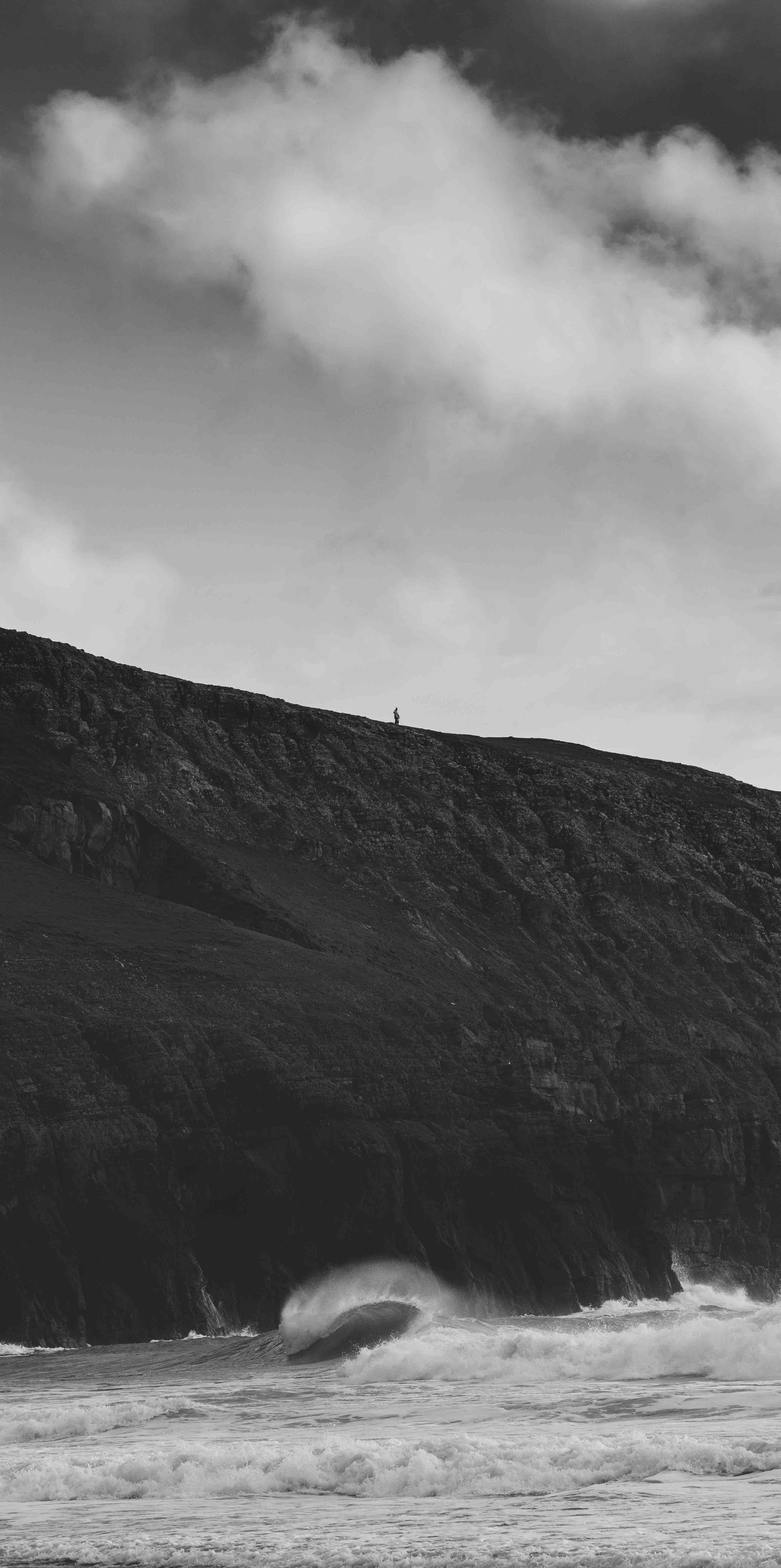 Black and white photo of a solitary silhouette on a cliff above ocean waves.