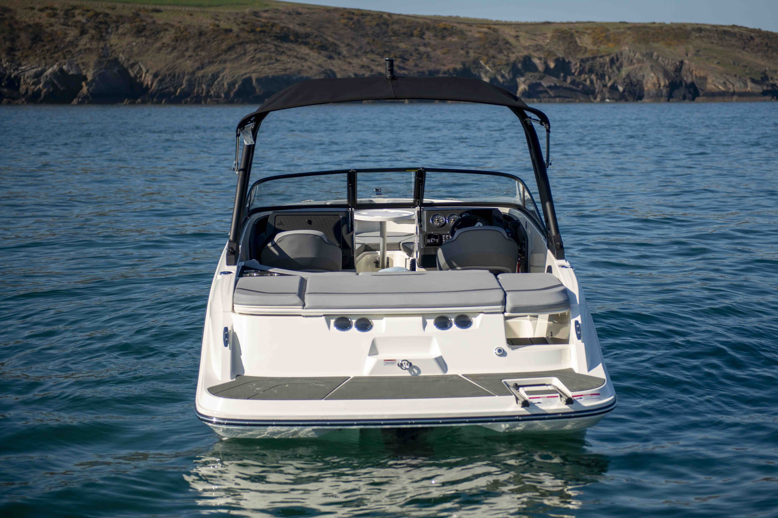 Rear view of a motorboat on the water with rocky shoreline in the background