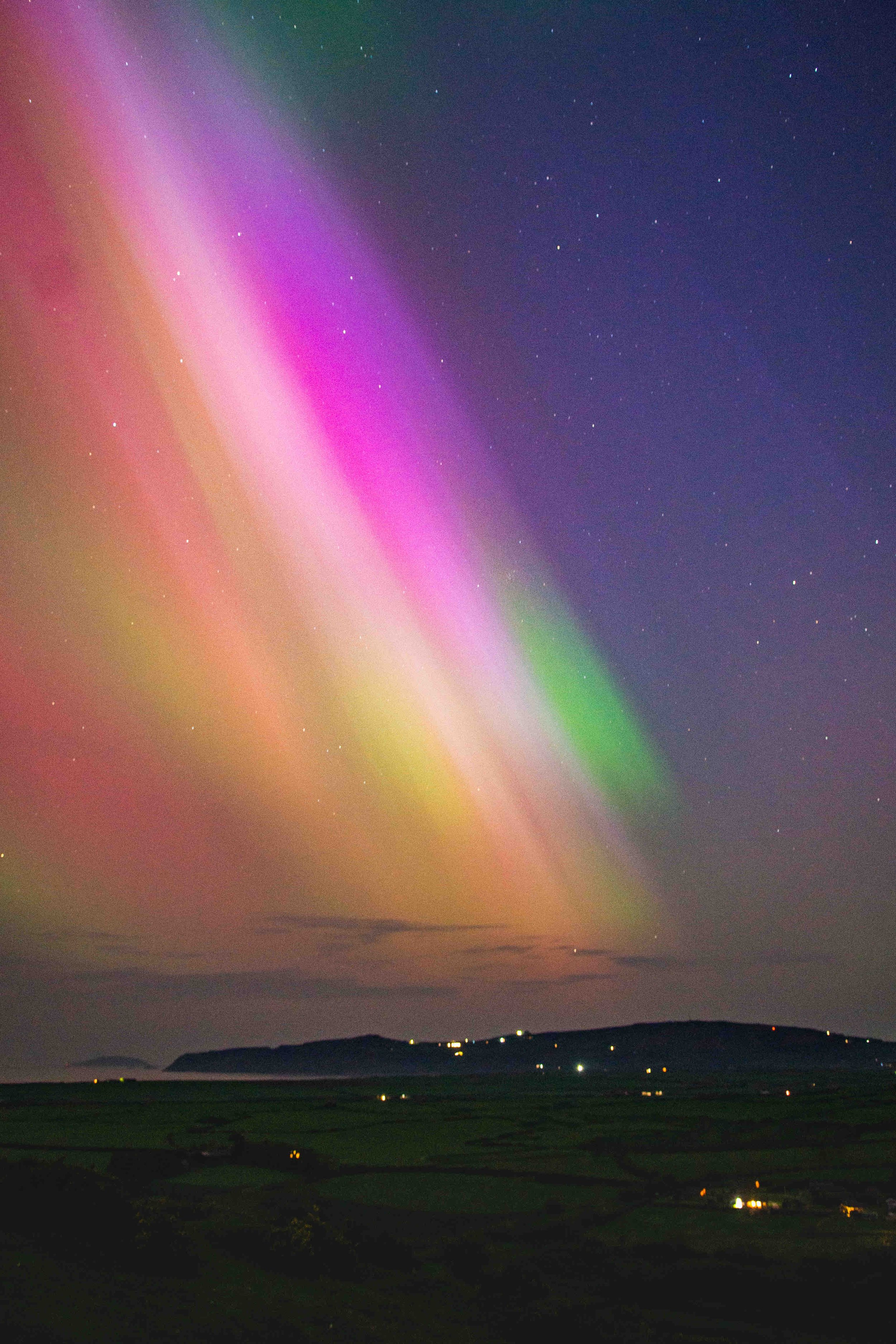 Colorful aurora borealis over a landscape with scattered lights at night.