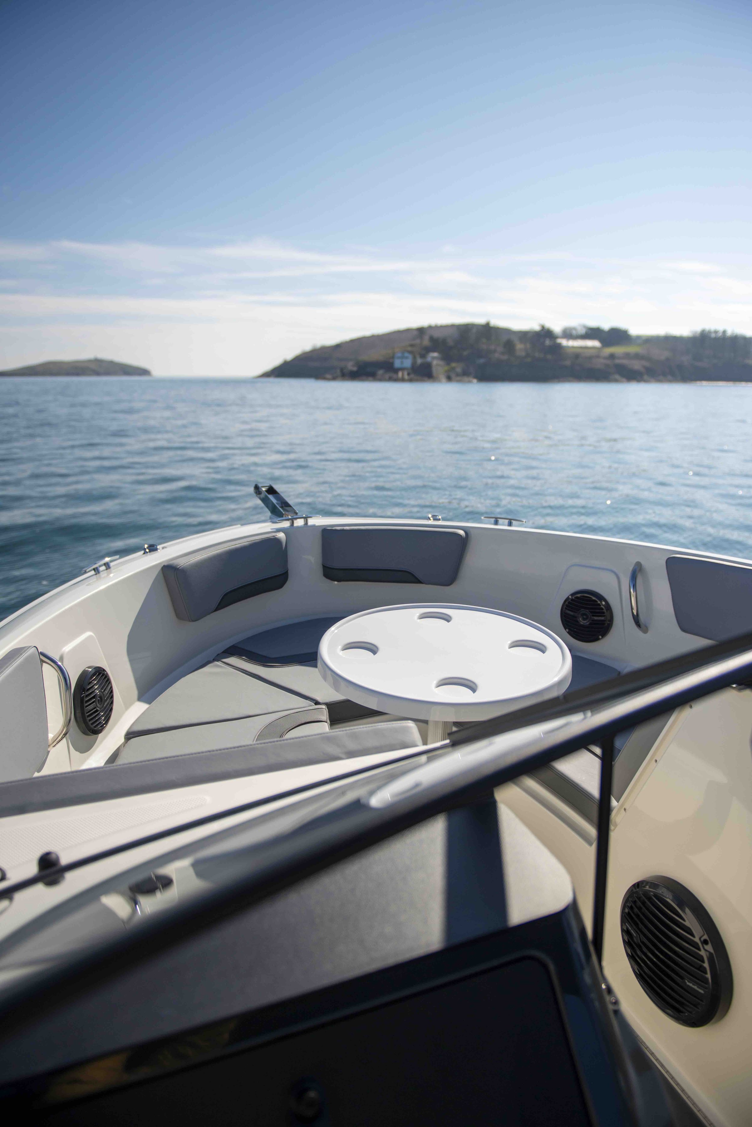 Interior of a boat with a circular table, seating area, and ocean view with distant hills.