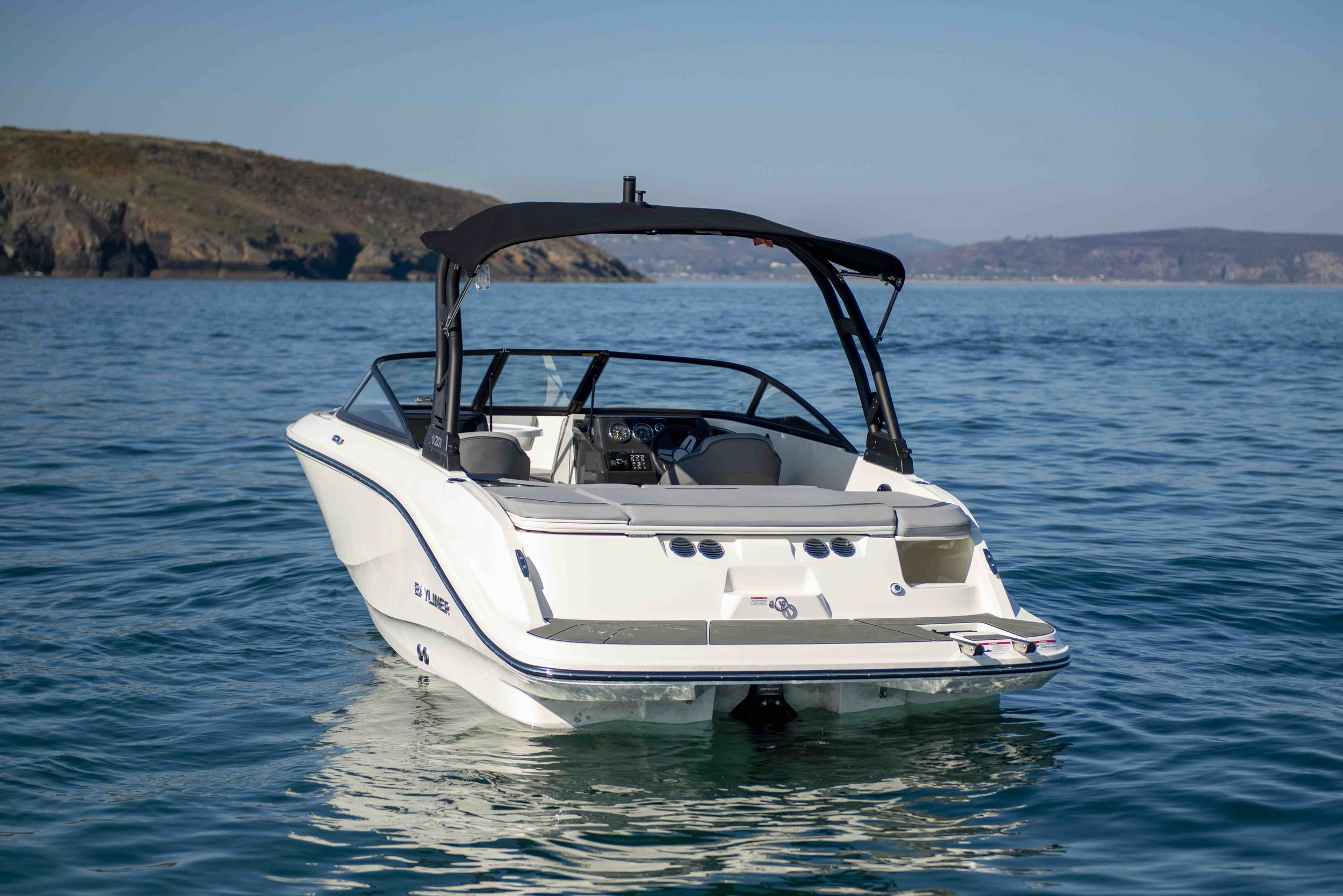 A white motorboat with a black canopy on a calm blue sea, with distant hills in the background.