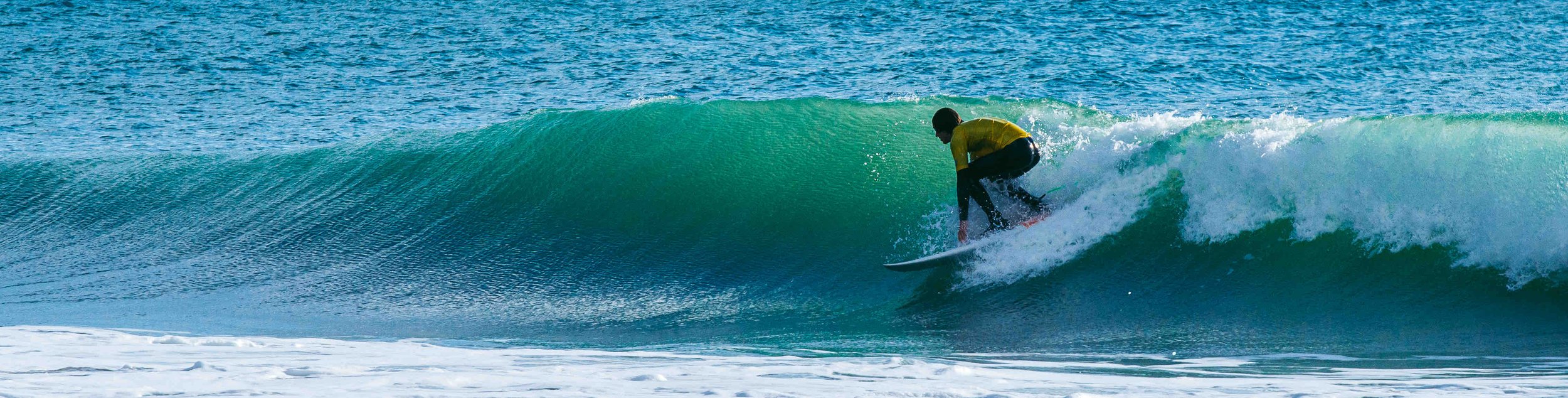 Surfer in yellow shirt riding a wave in the ocean.