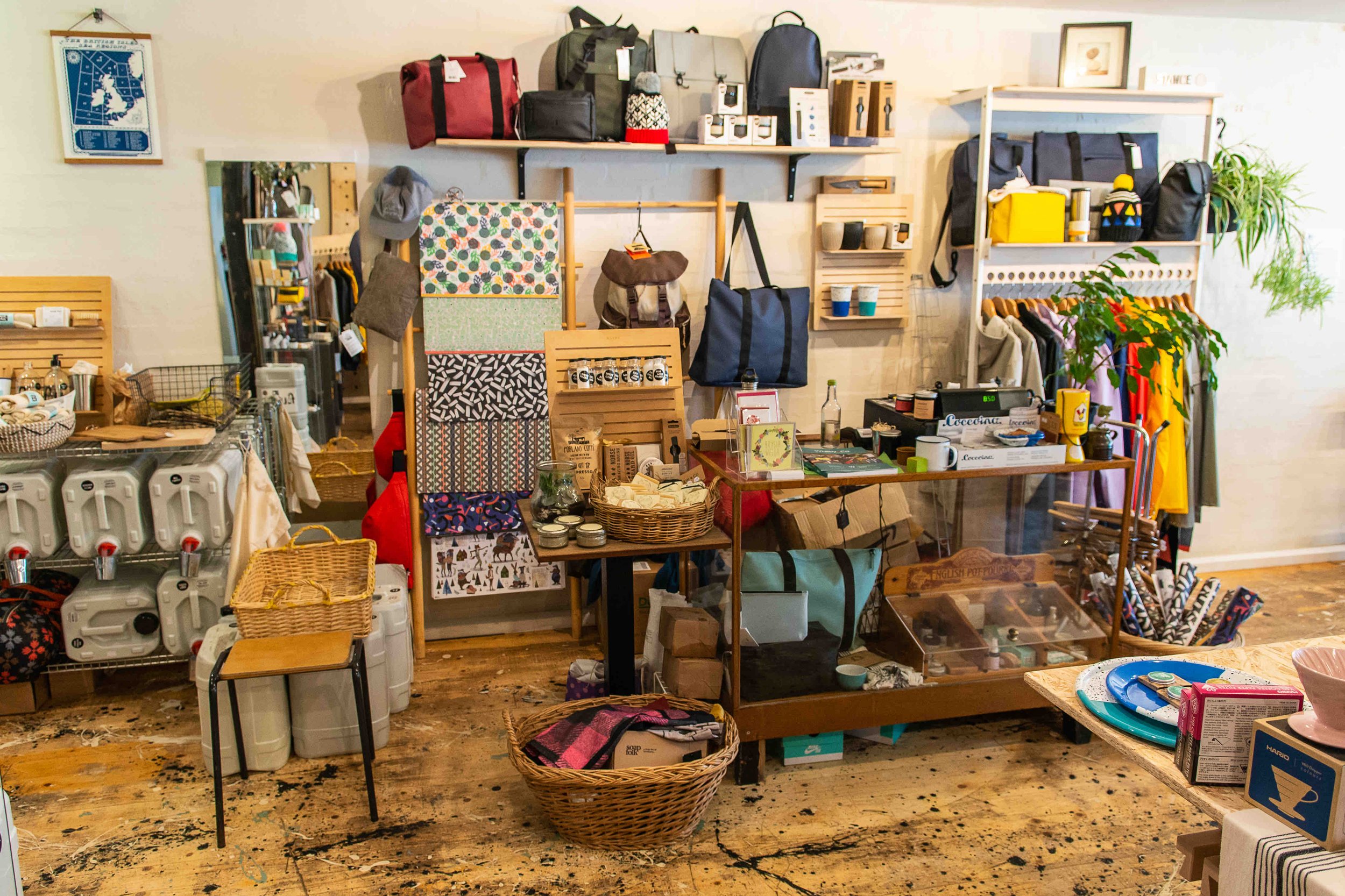 Interior of a small shop with shelves displaying various bags, colorful textiles, home goods, and clothing. The floor is wooden, and a variety of merchandise is organized in baskets, on racks, and tables.