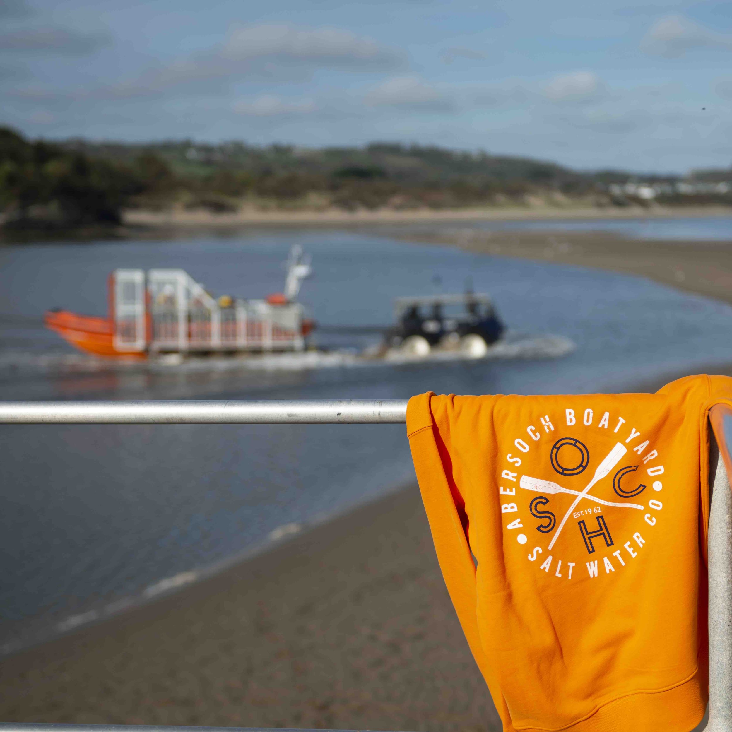 Orange hoodie draped over railing near boat and tractor in waterway.