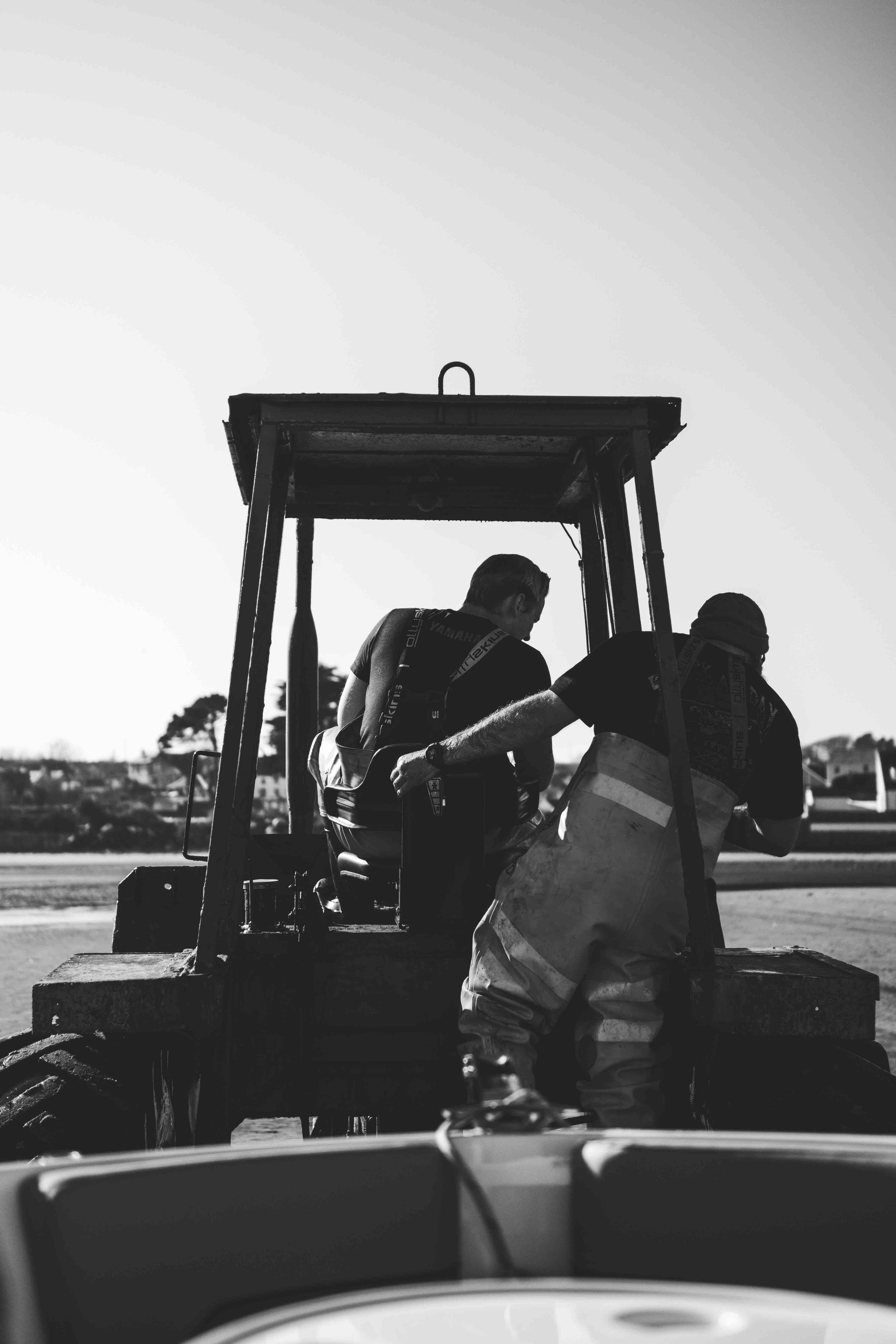 Two people working on a tractor outdoors in a black and white photograph.
