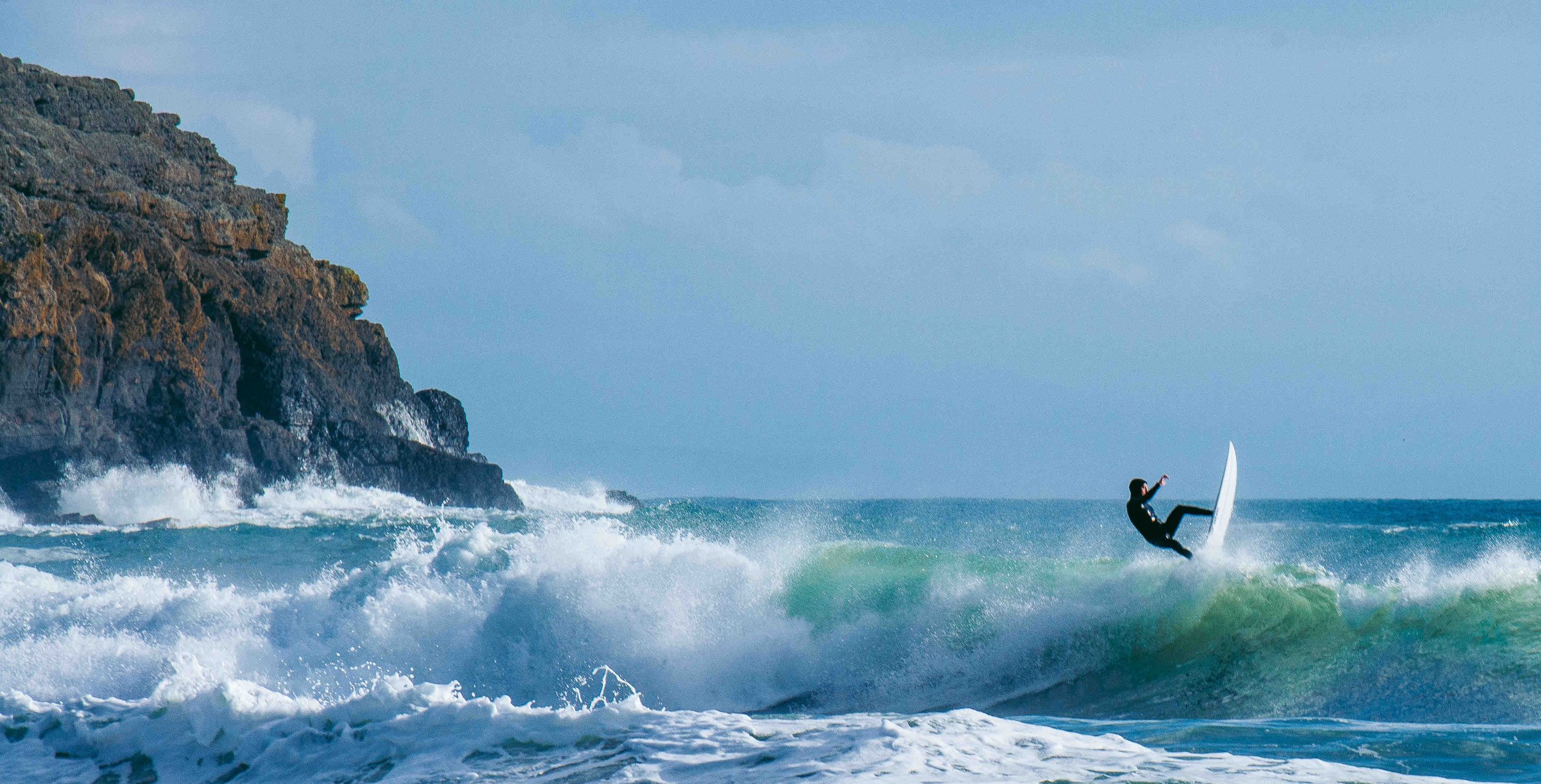 Surfer performing on a wave near a rocky coastline