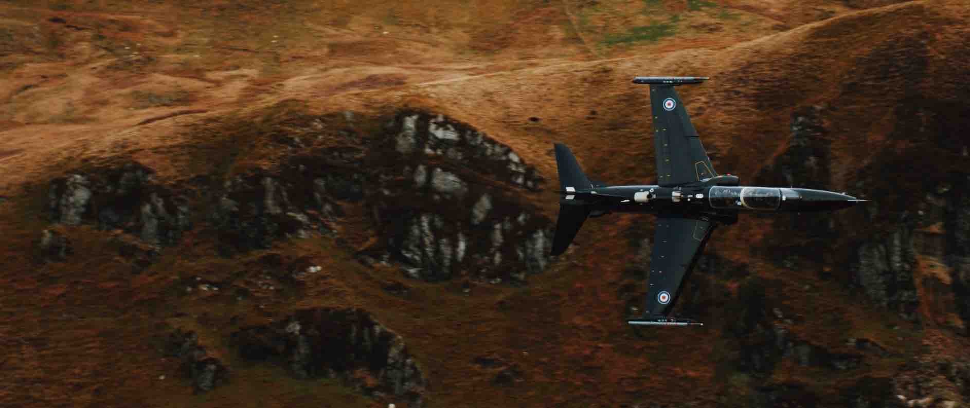 Military jet flying over a rocky terrain