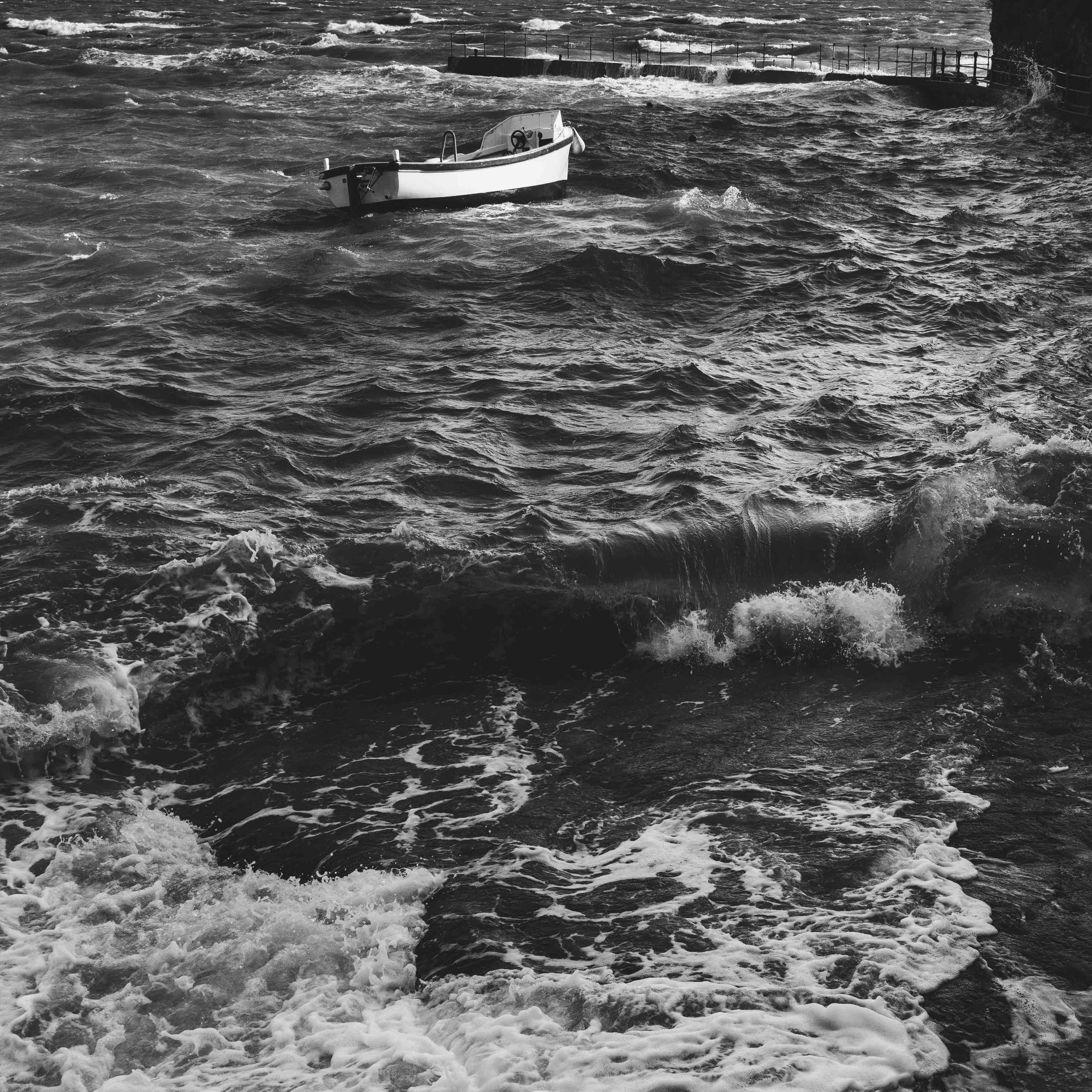 Boat on rough sea waves in black and white, dark clouds overhead