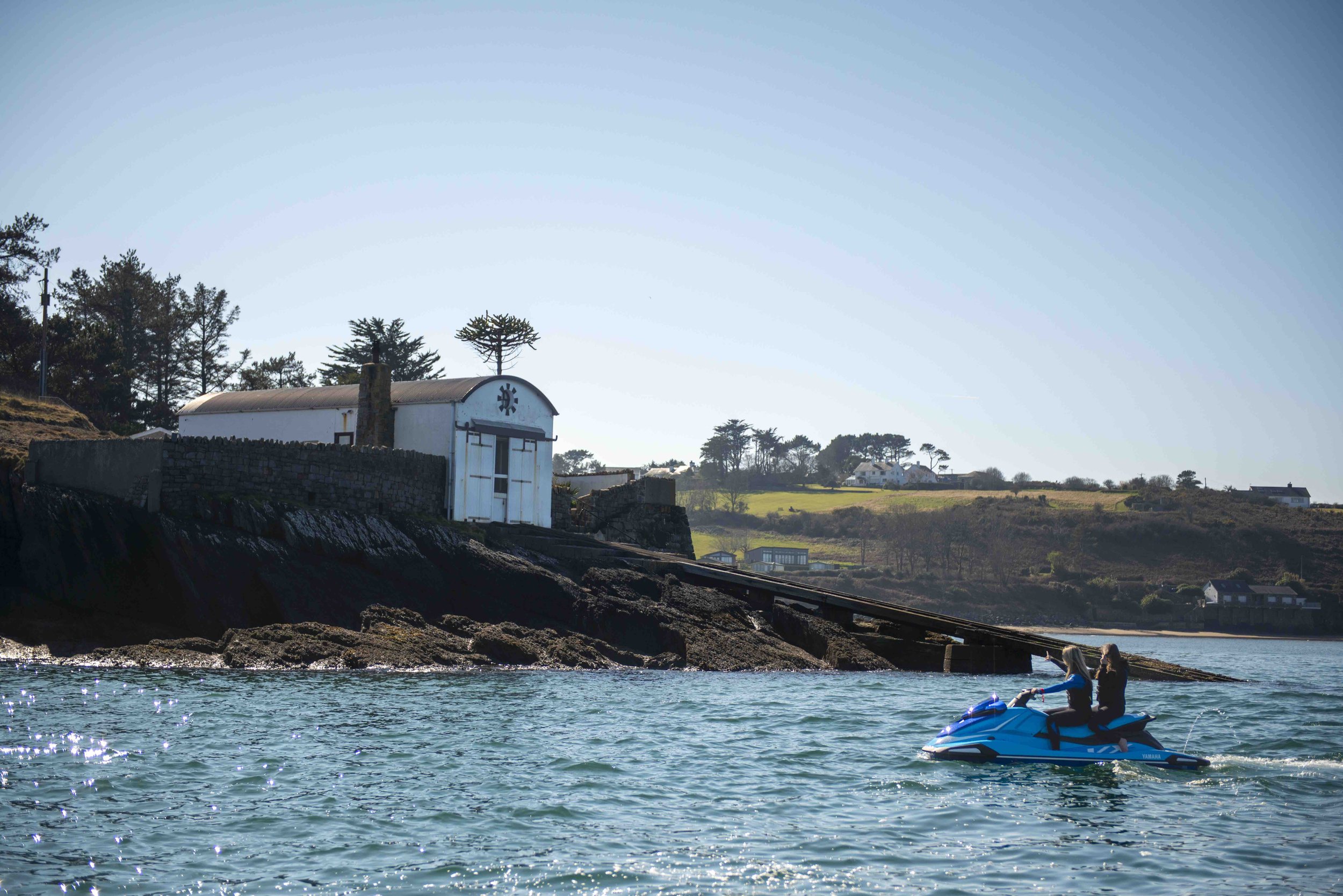 Building on a rocky cliff by the sea with a person riding a jet ski.