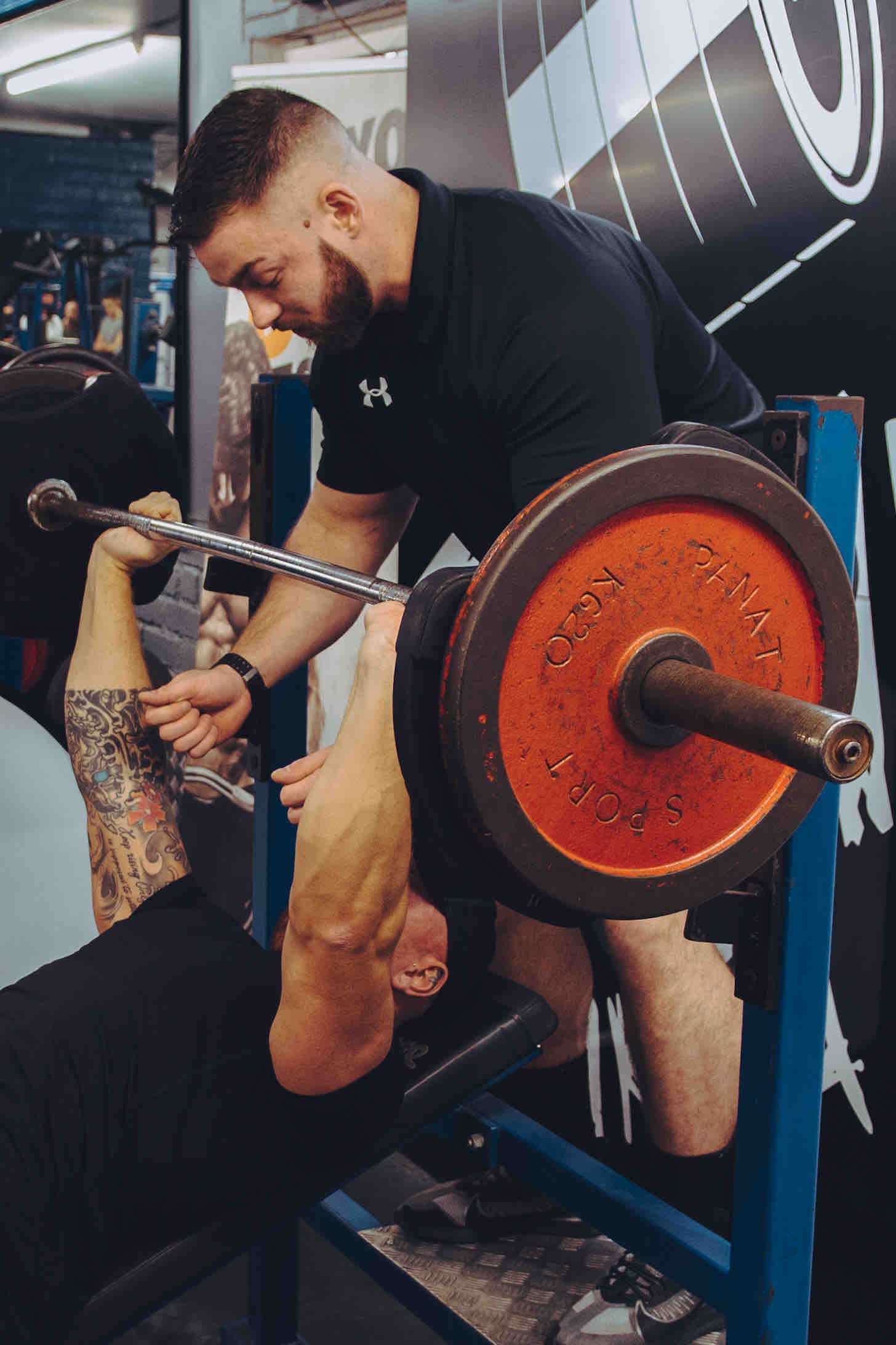 Man bench pressing with assistance in a gym