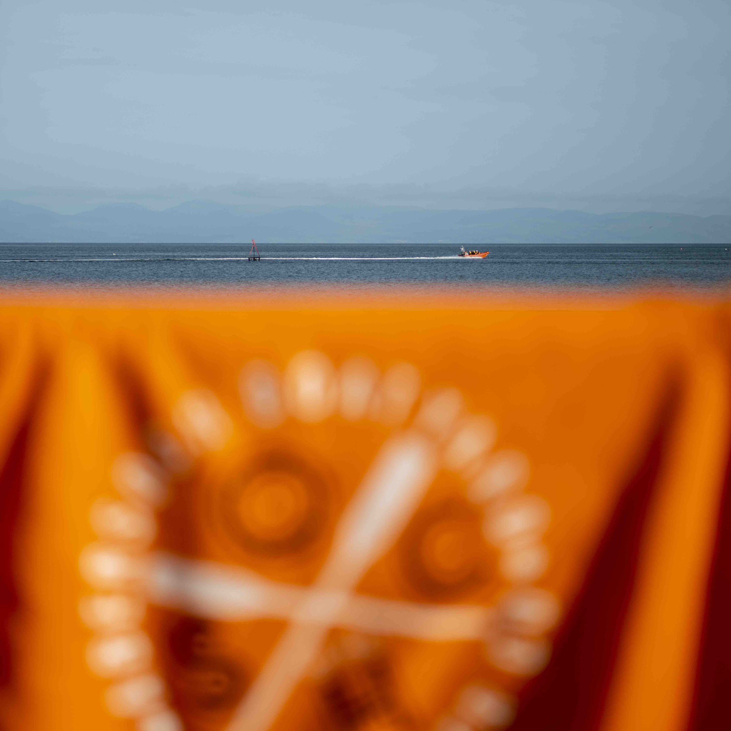 Blurred orange towel or flag in foreground with ocean and small boat in background
