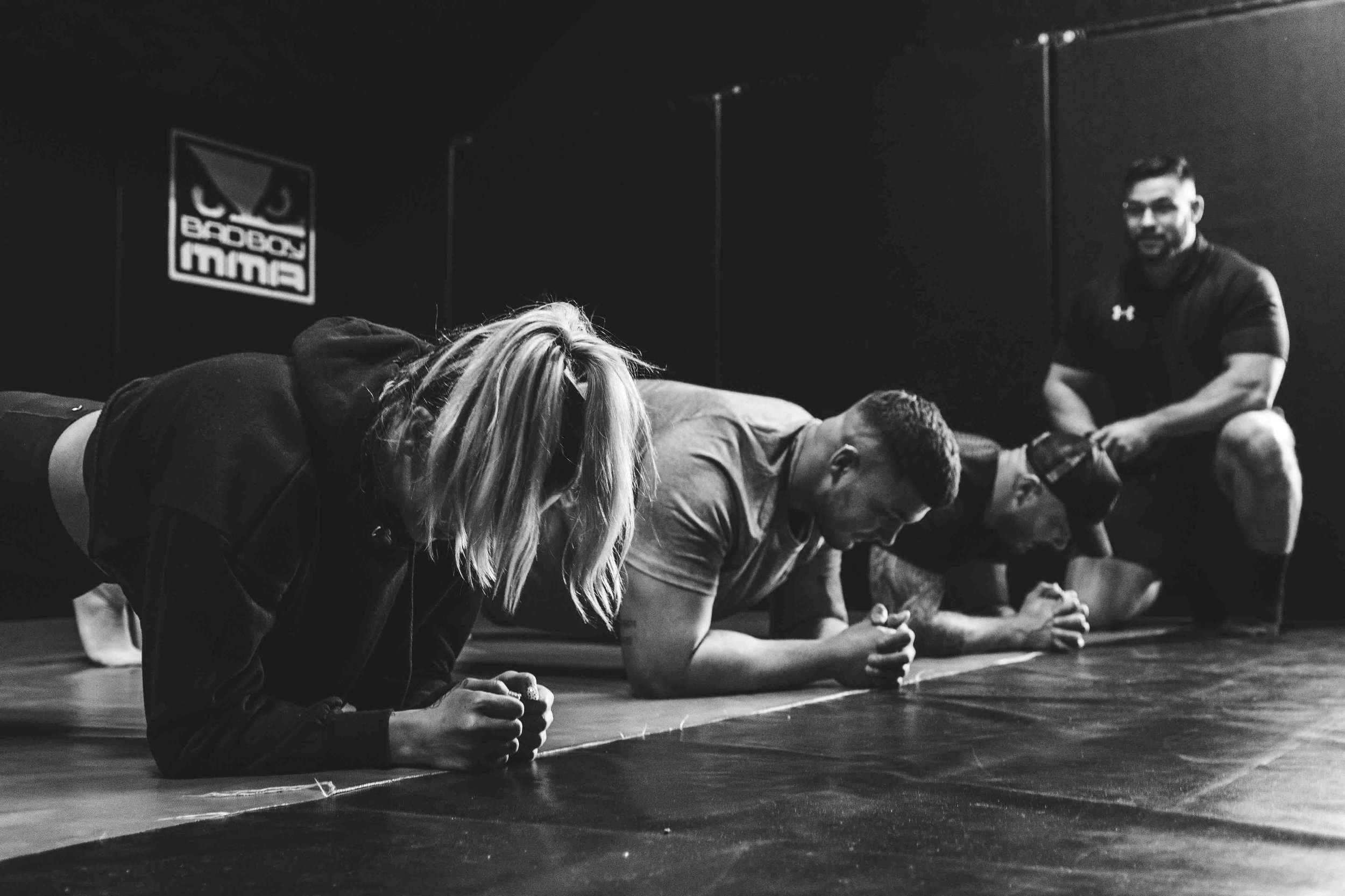 Group of people doing planks in a gym with a trainer coaching them.