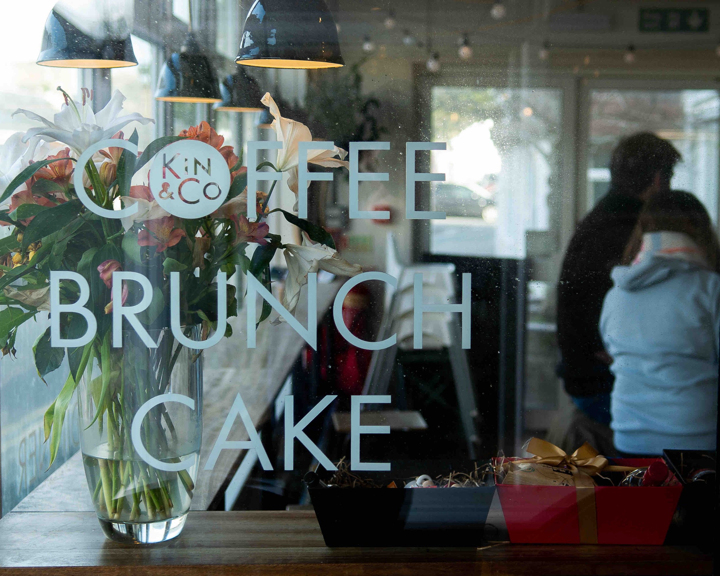 Cafe window with 'Coffee Brunch Cake' signs and flowers inside