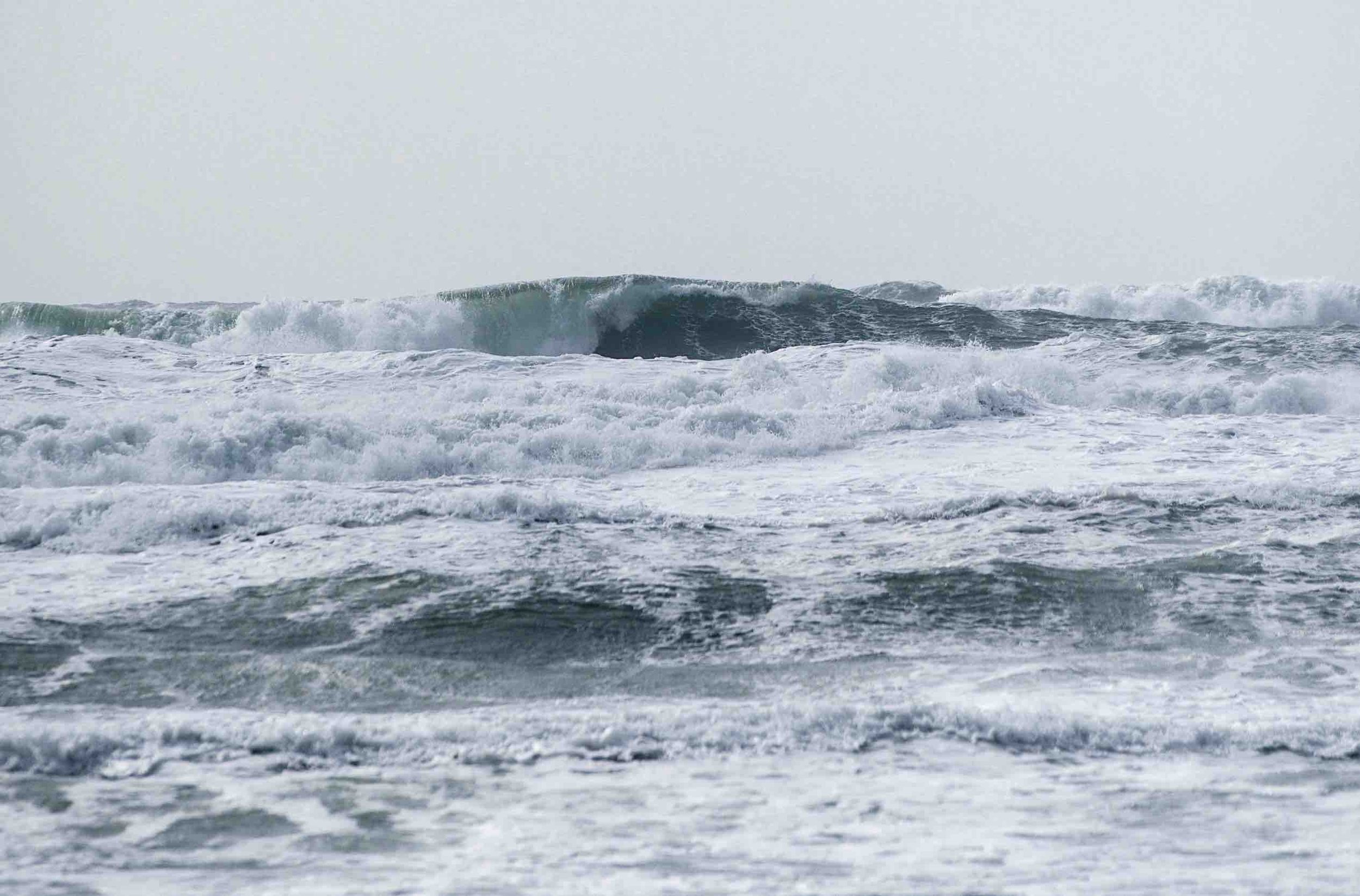 Rough ocean waves crashing with white foam under a cloudy sky.