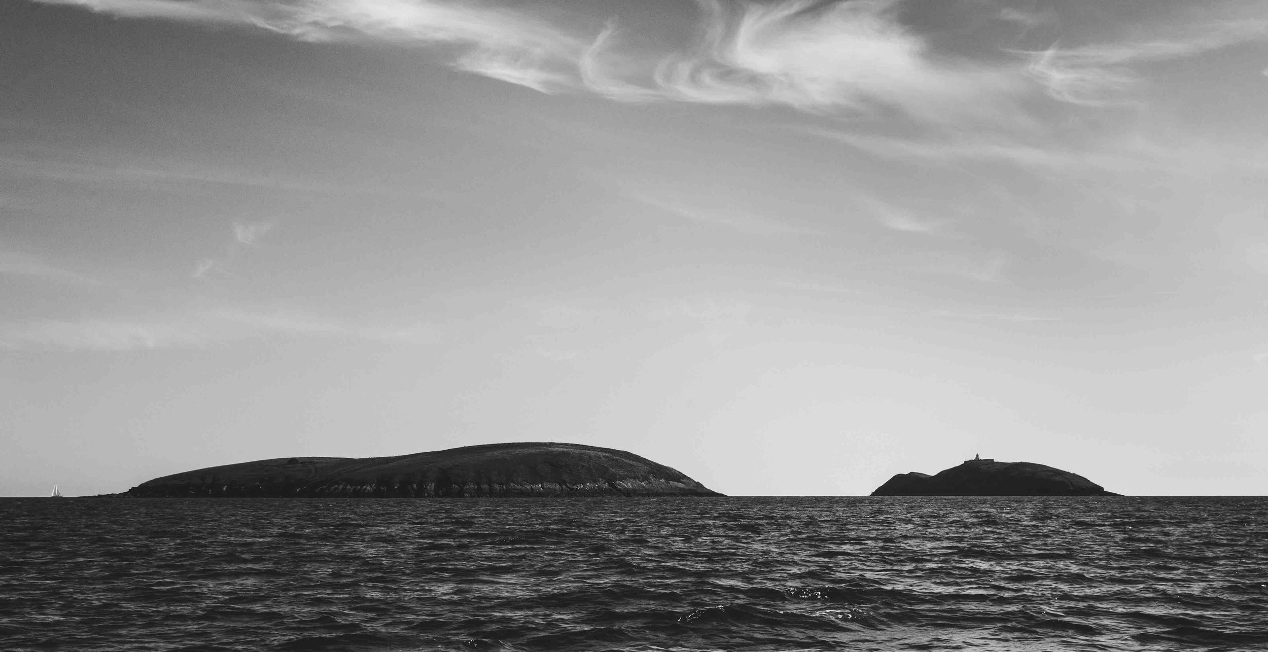 Black and white seascape with two small islands and cloudy sky.