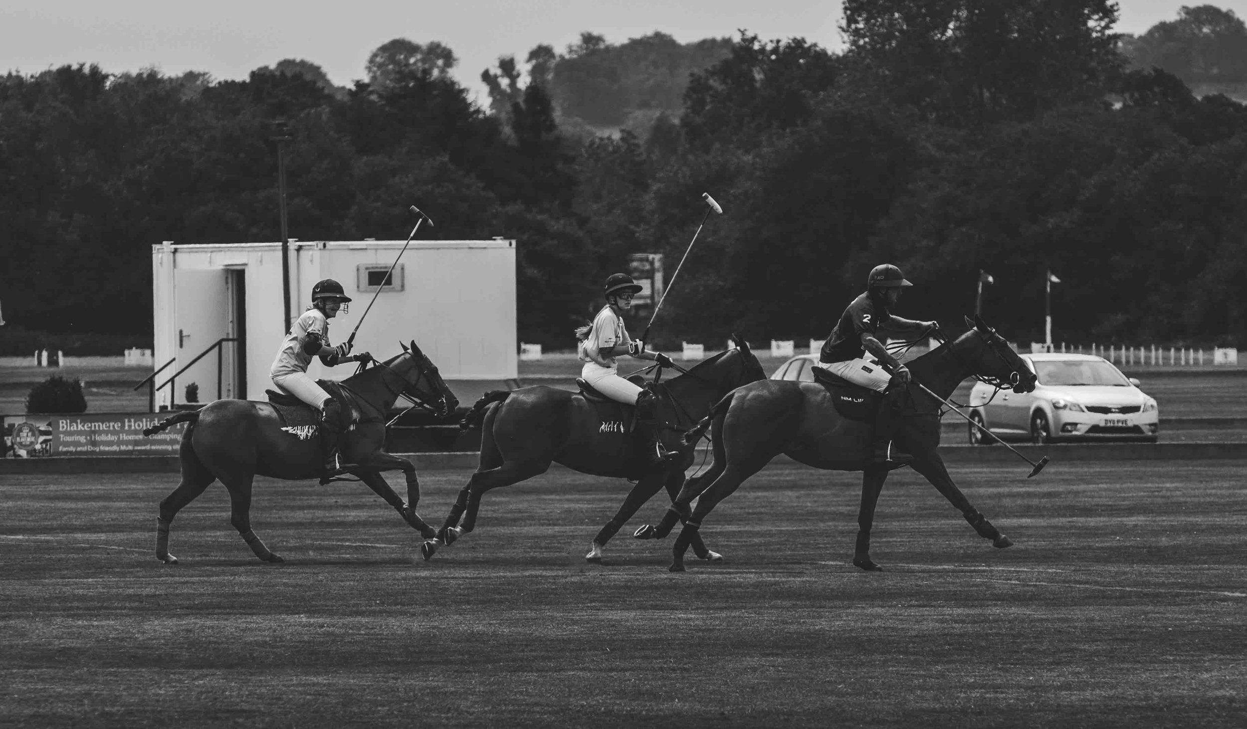 Black and white photo of polo players riding horses on a field during a match.
