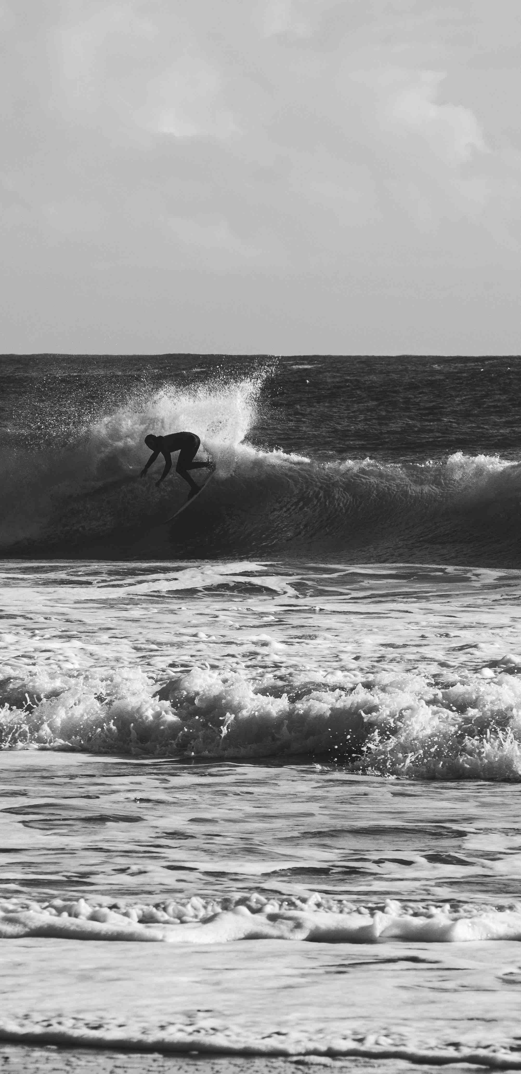 Silhouette of a surfer riding a wave in black and white photo.
