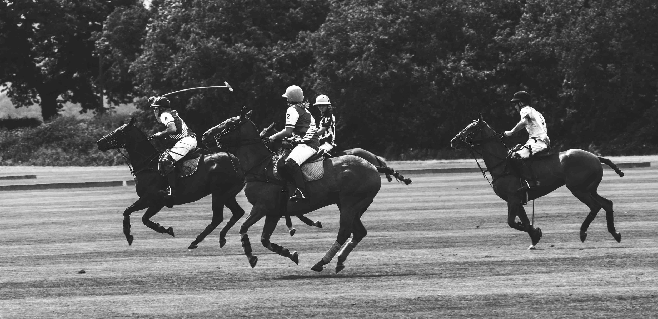 Black and white image of a polo match with four players on horseback on a field.