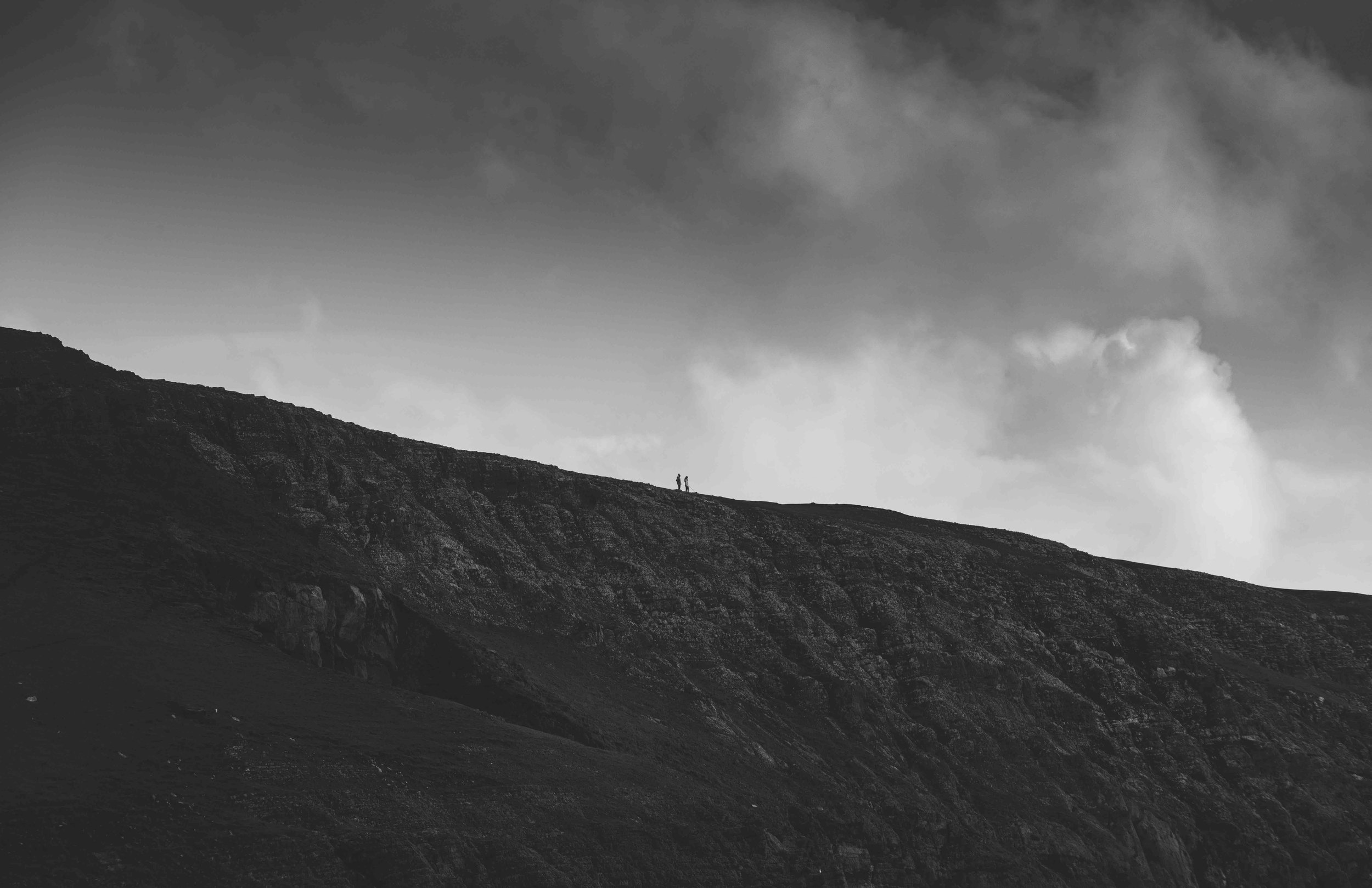 Two hikers on a rocky hill under a cloudy sky, black and white photo.
