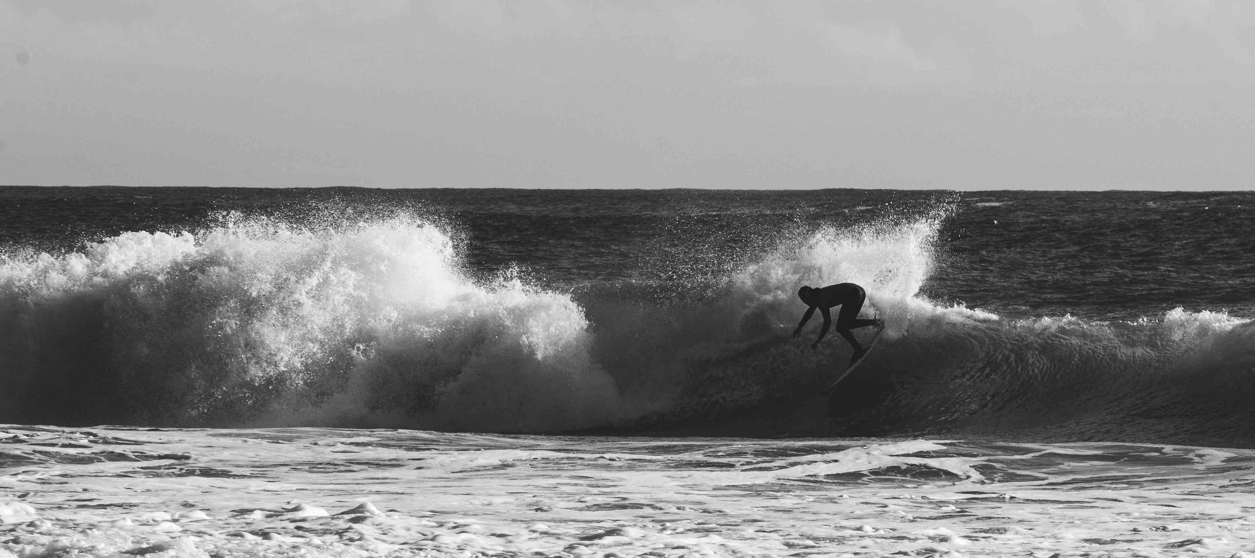 Black and white photo of a surfer riding a wave at sea.
