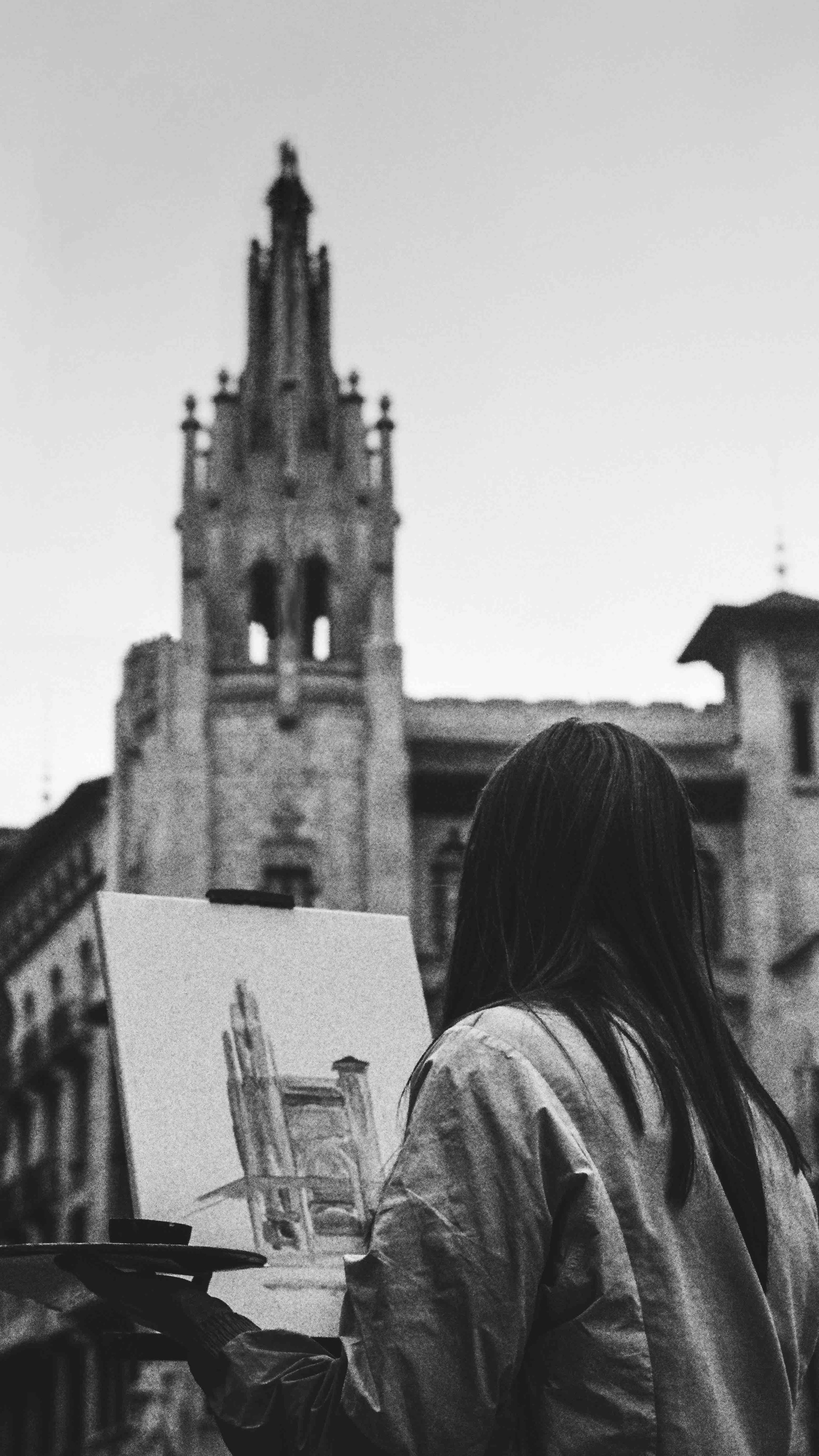 Person painting a gothic-style building outdoors, focused on architectural details, in grayscale.
