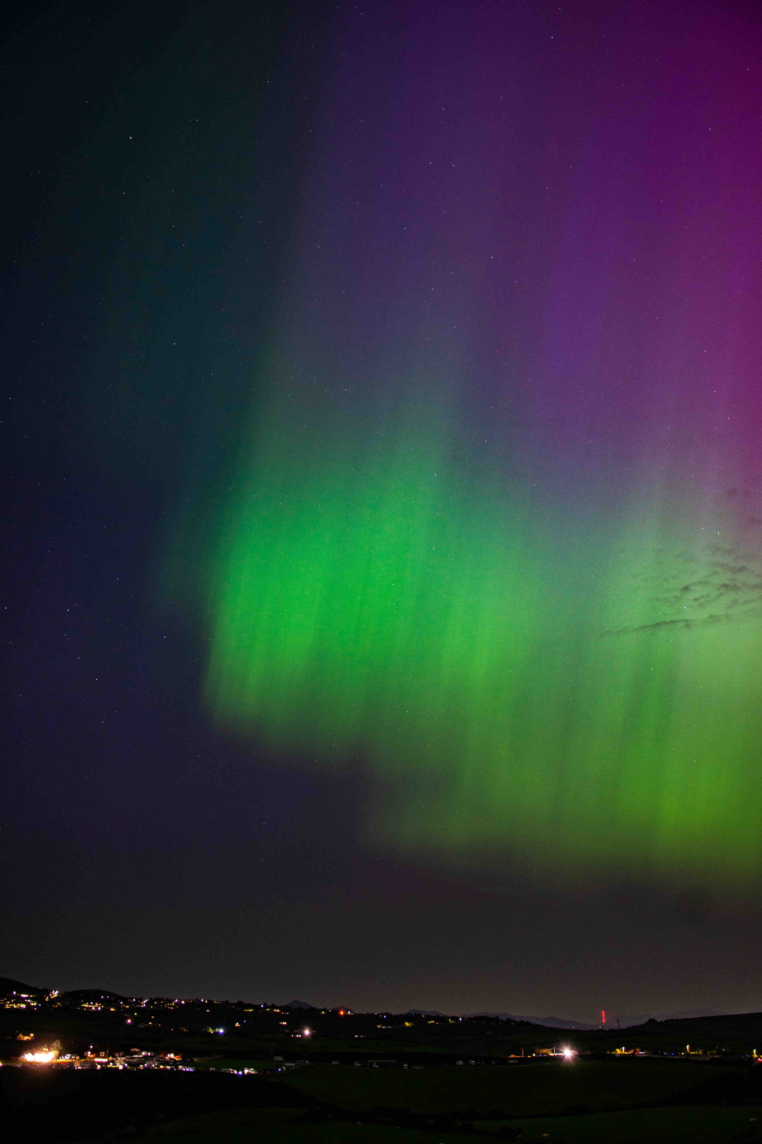 Aurora borealis with green and purple hues over a landscape at night.