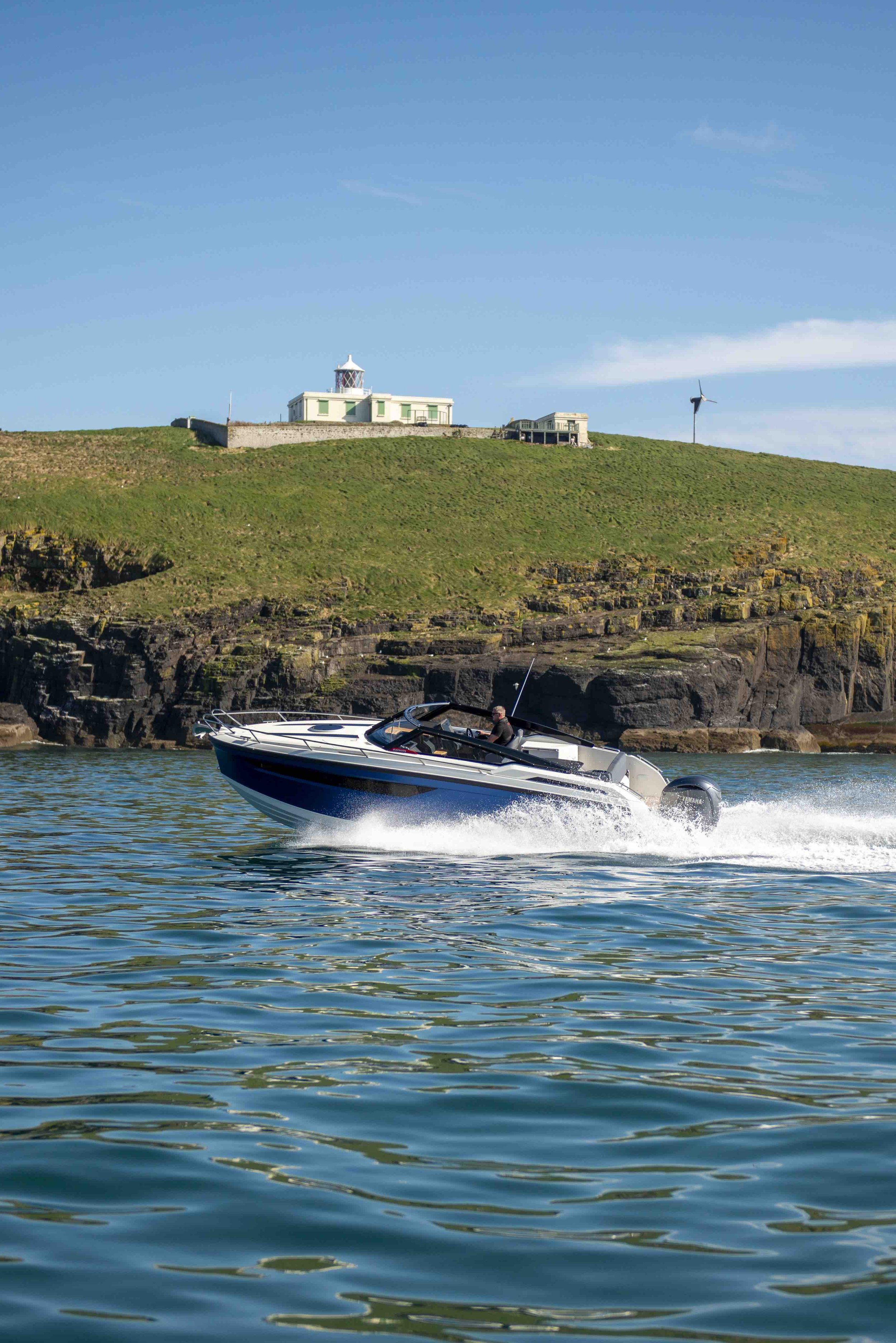 Speedboat on water with coastal landscape and lighthouse in the background