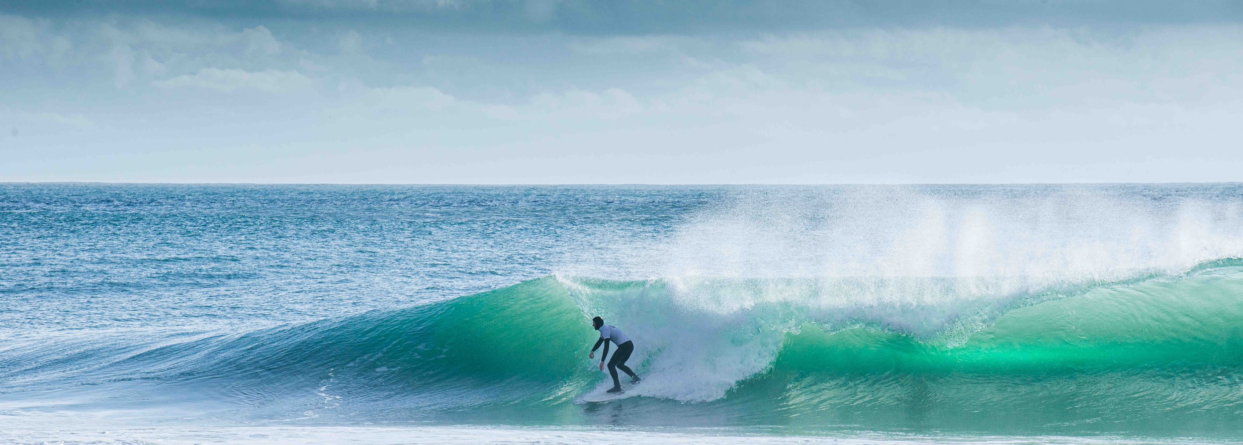 Surfer riding a wave in the ocean under a cloudy sky.