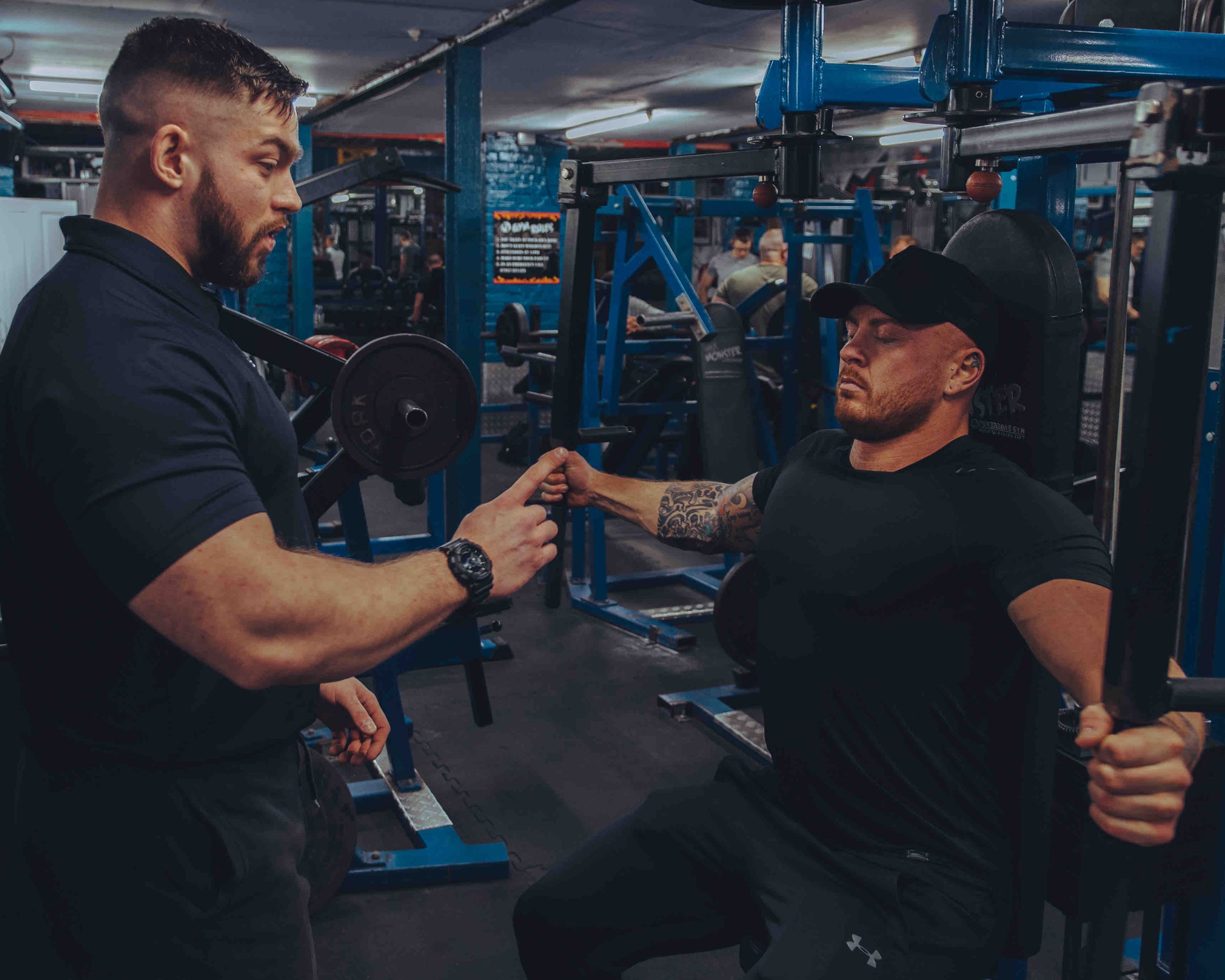 A fitness trainer instructing a man using a chest press machine in a gym.