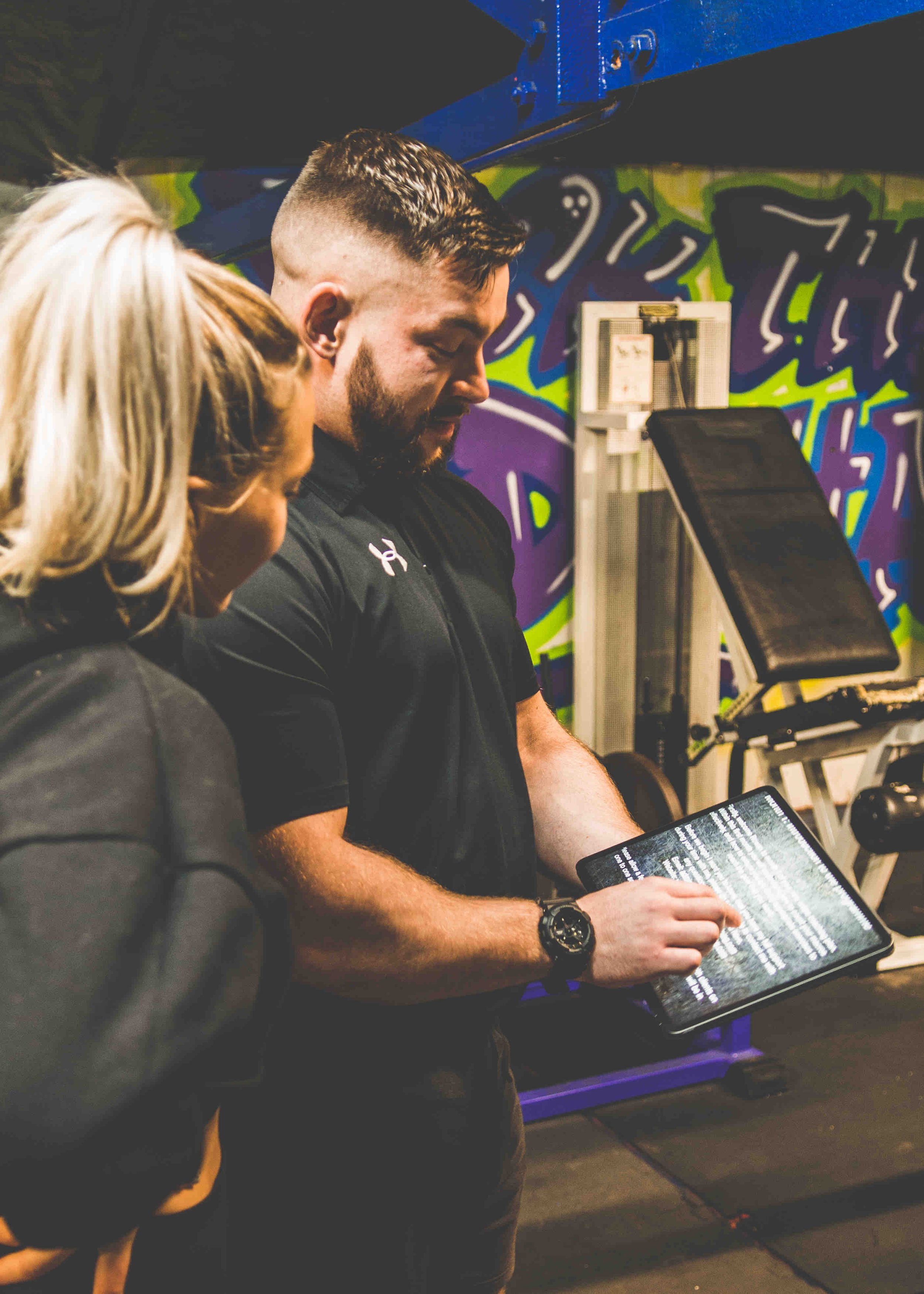 A fitness trainer showing a workout plan on a digital tablet to a gym member.