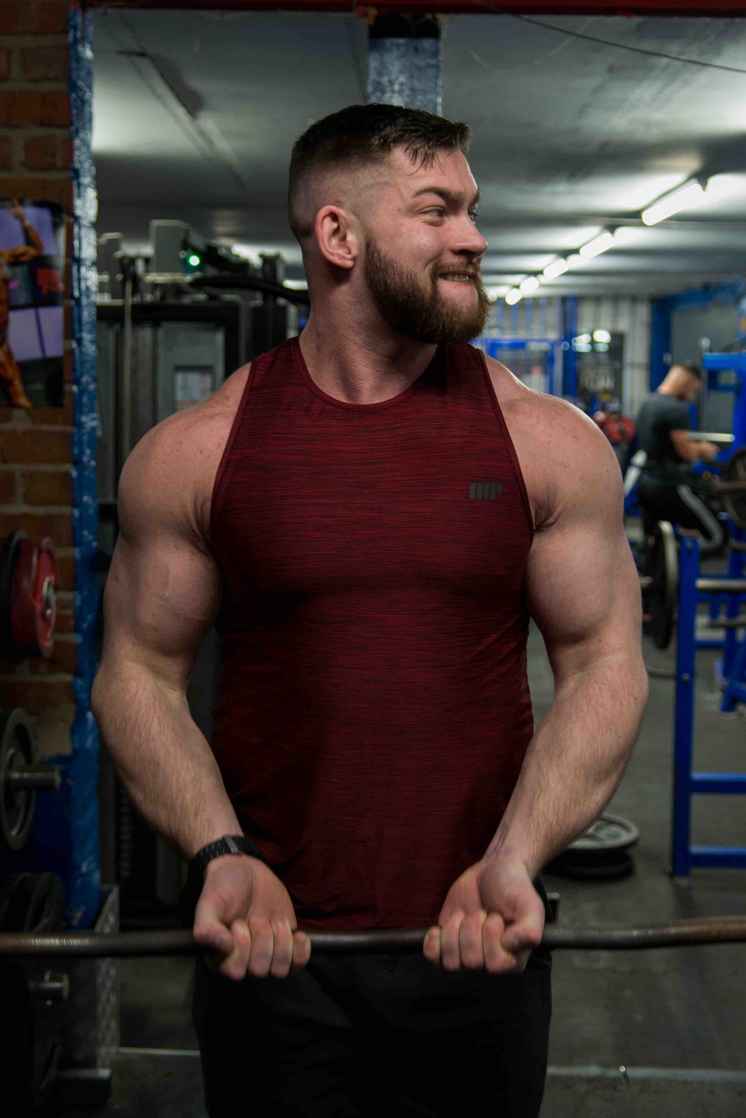 Man in a gym lifting weights wearing a red tank top.