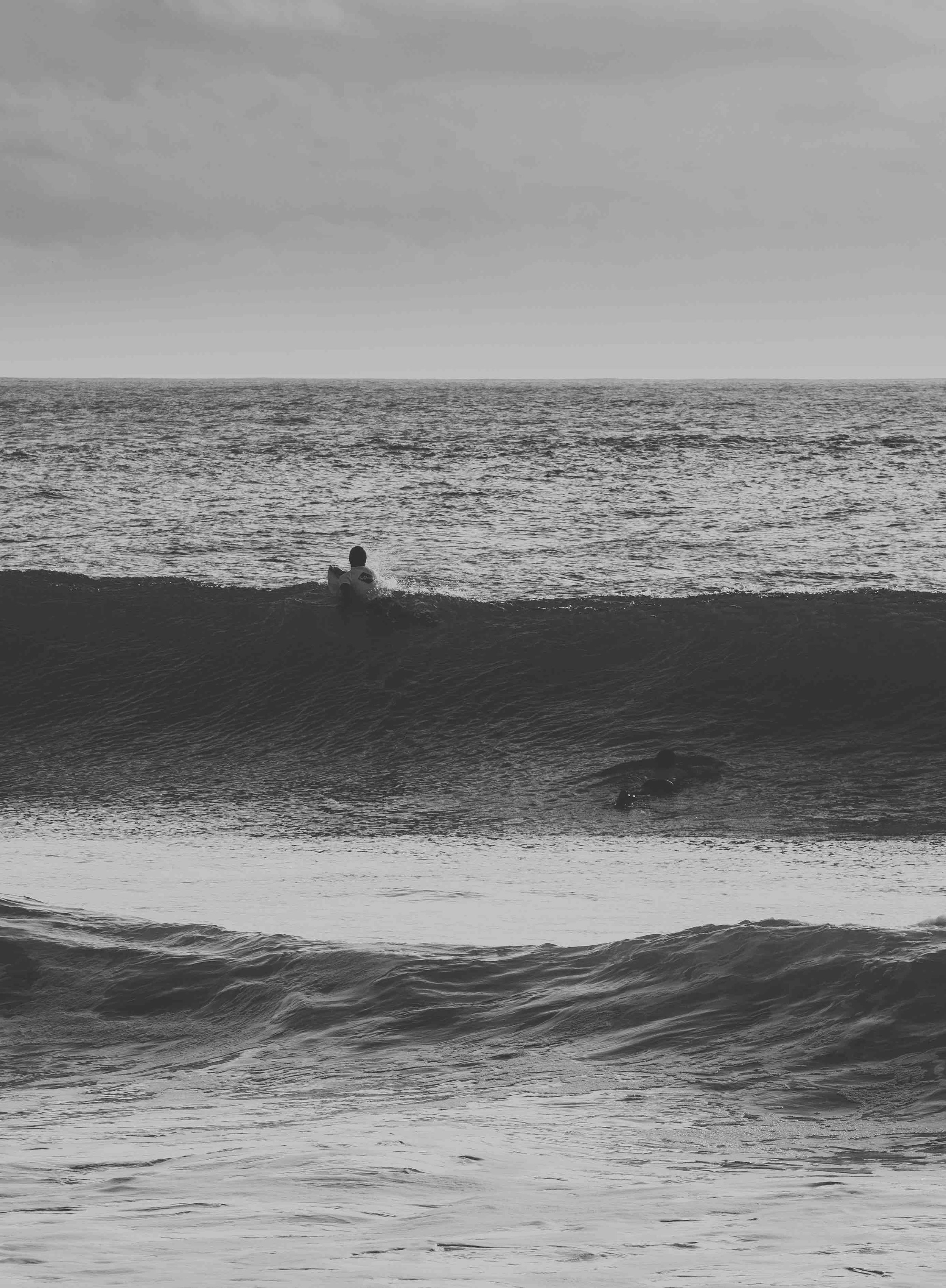 Monochrome photo of surfers riding waves in the ocean.
