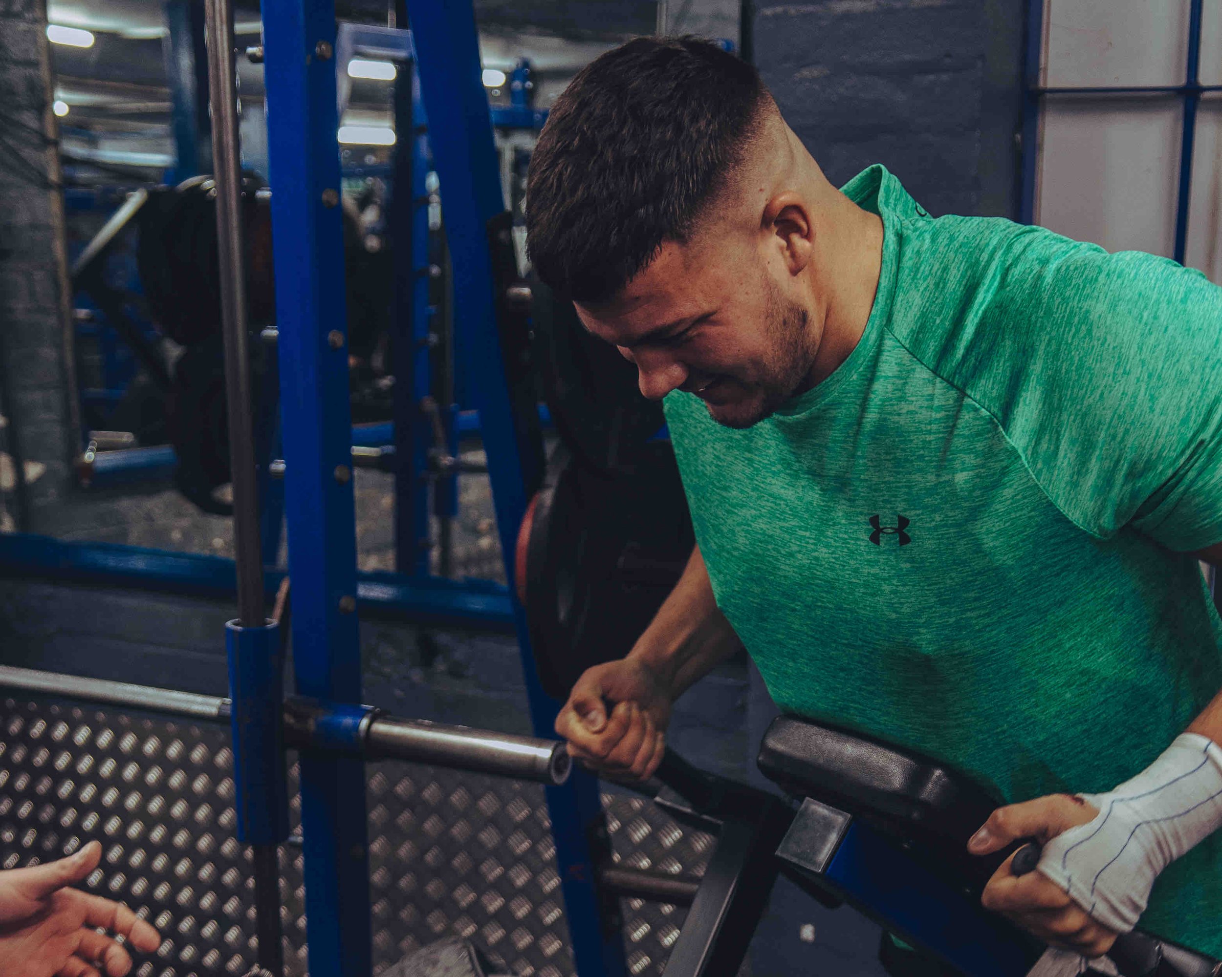 Person in gym wearing a green shirt lifting weights on a machine.