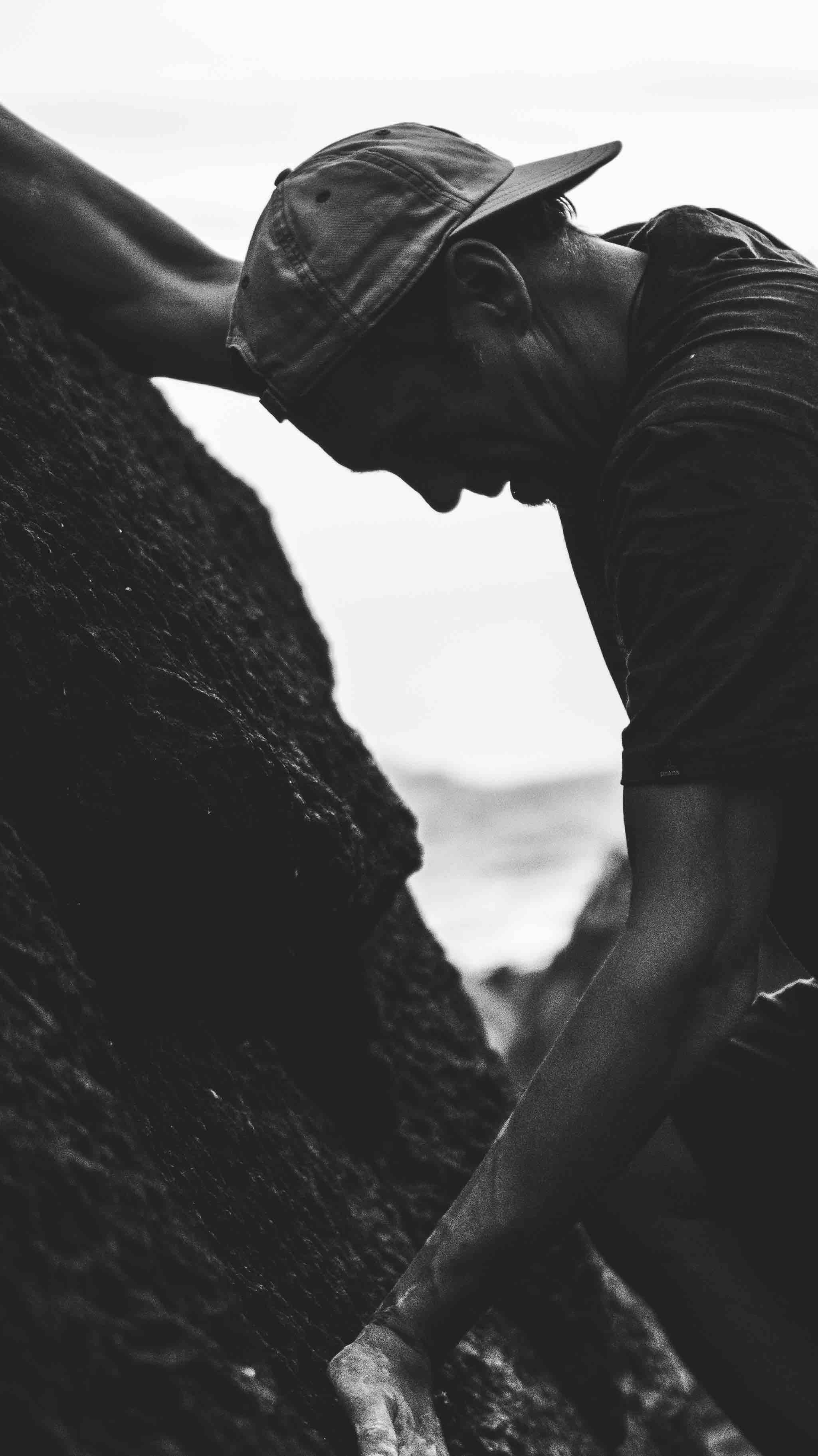 Silhouette of a person rock climbing with a cap, against a clear sky background.