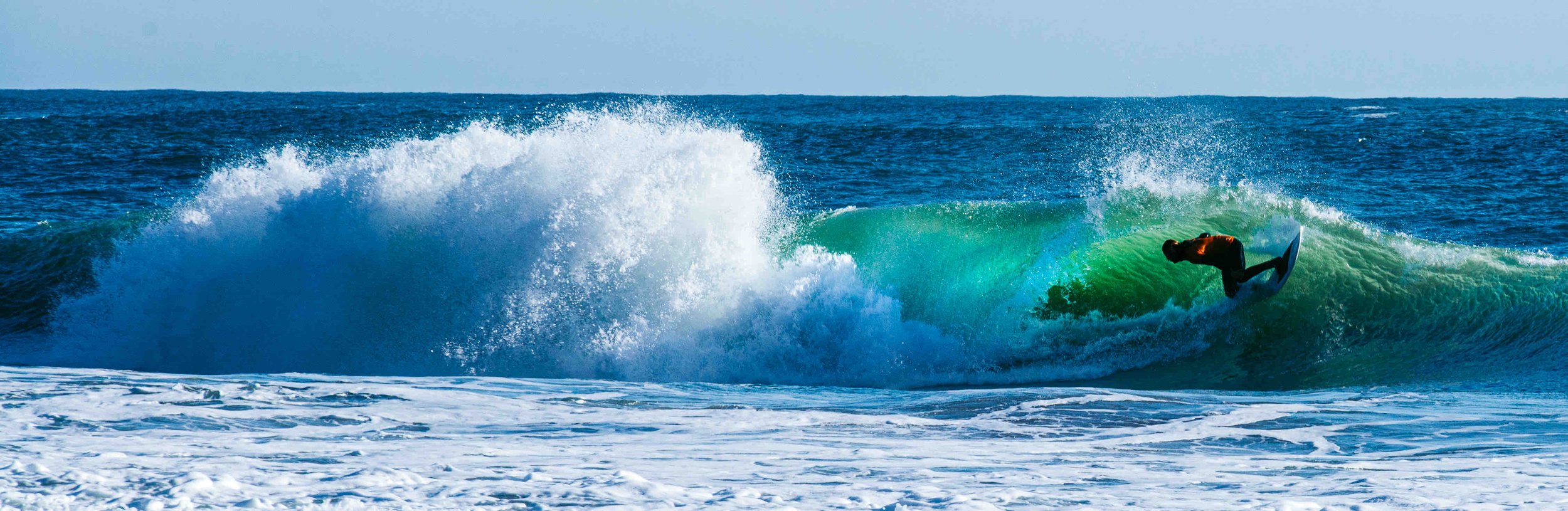Surfer riding inside a crashing ocean wave on a sunny day.