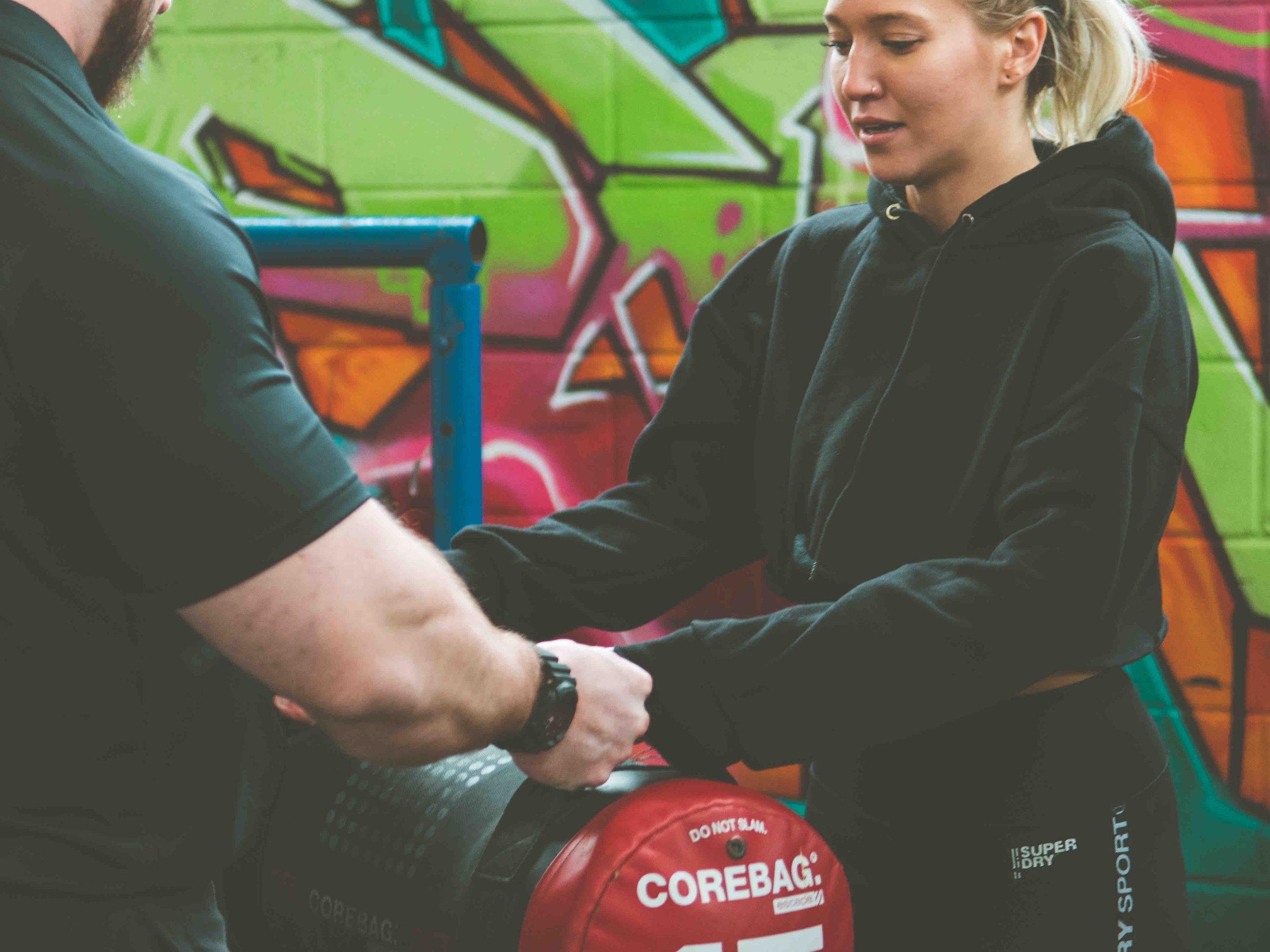Two people in a gym with a Corebag; one has outstretched hands.
