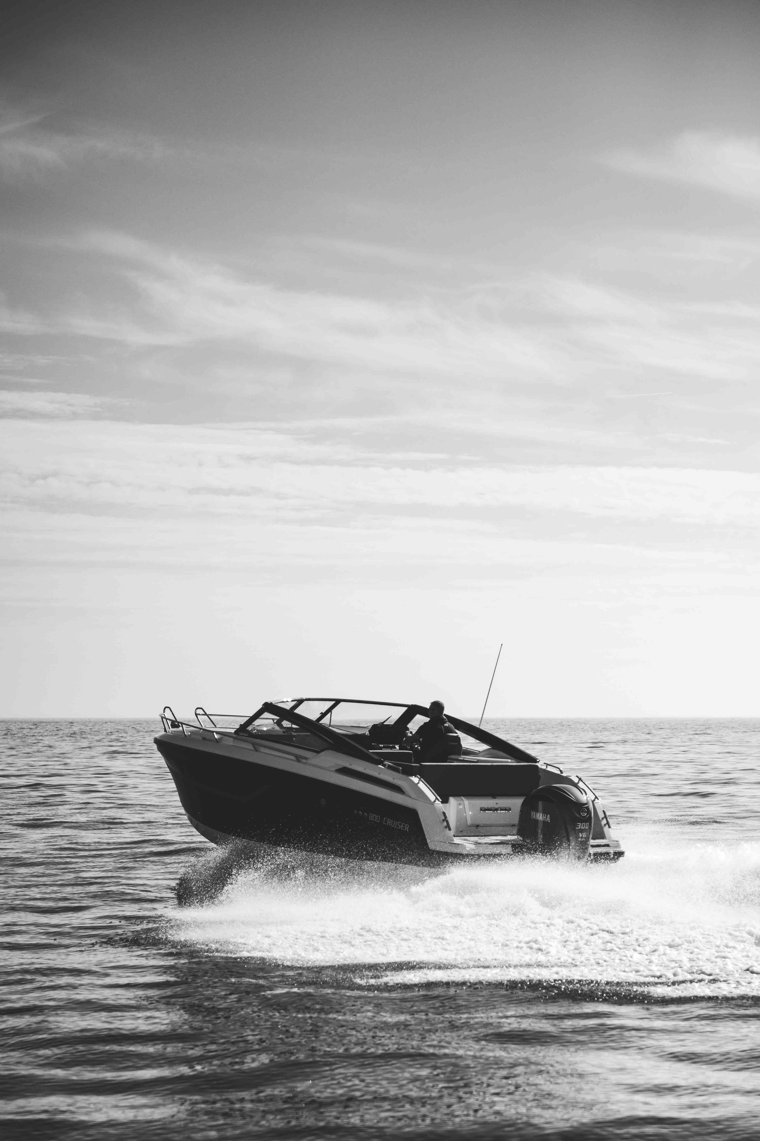 Black and white image of a speedboat on the ocean, with a person driving it and creating a wake.